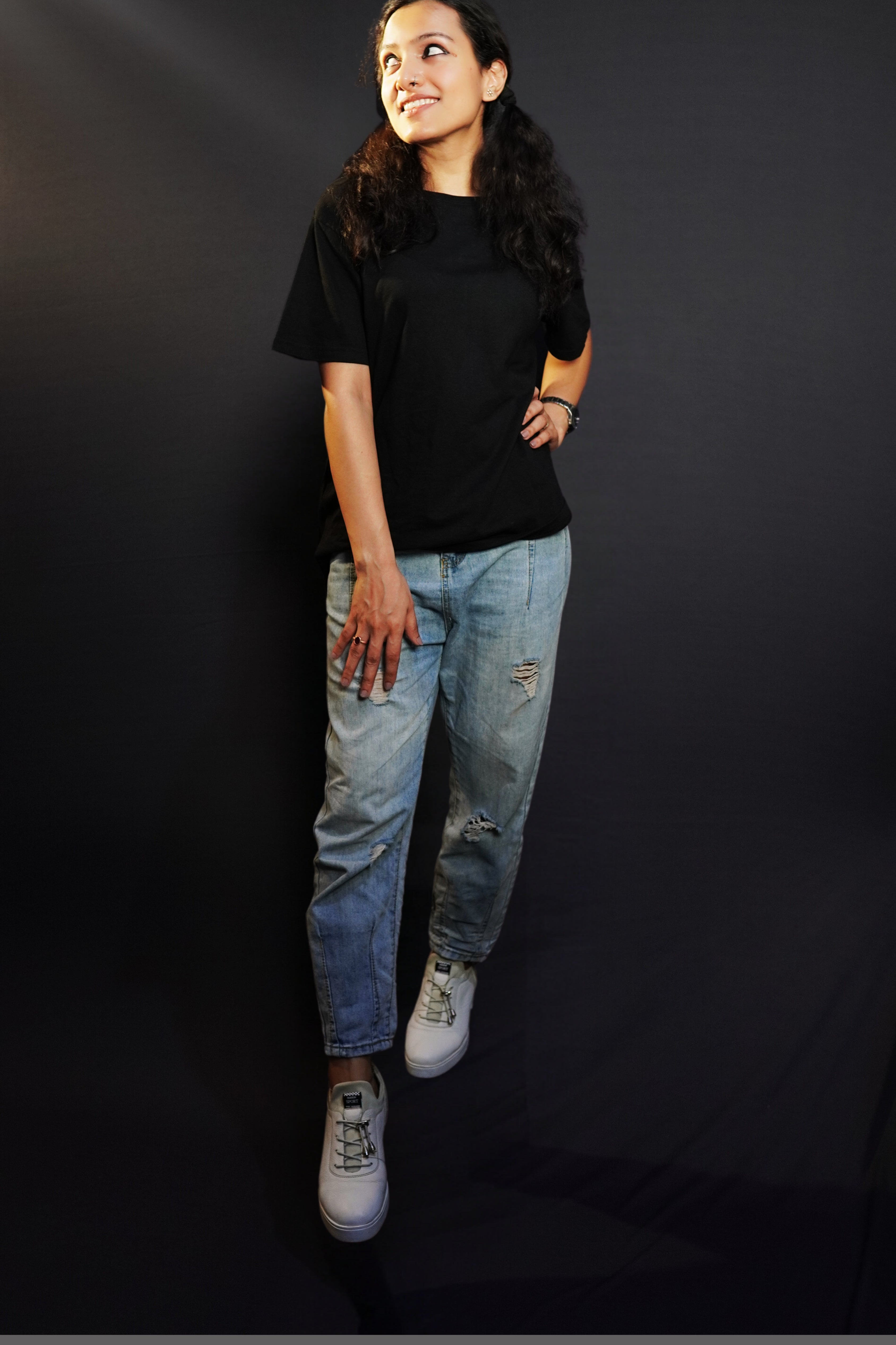 An elegant model wearing a short sleeved long length plain midnight black women's t-shirt, looking sideways as her hand gently lies on her waist and thigh, highlighting a stylish modern look-Muselot