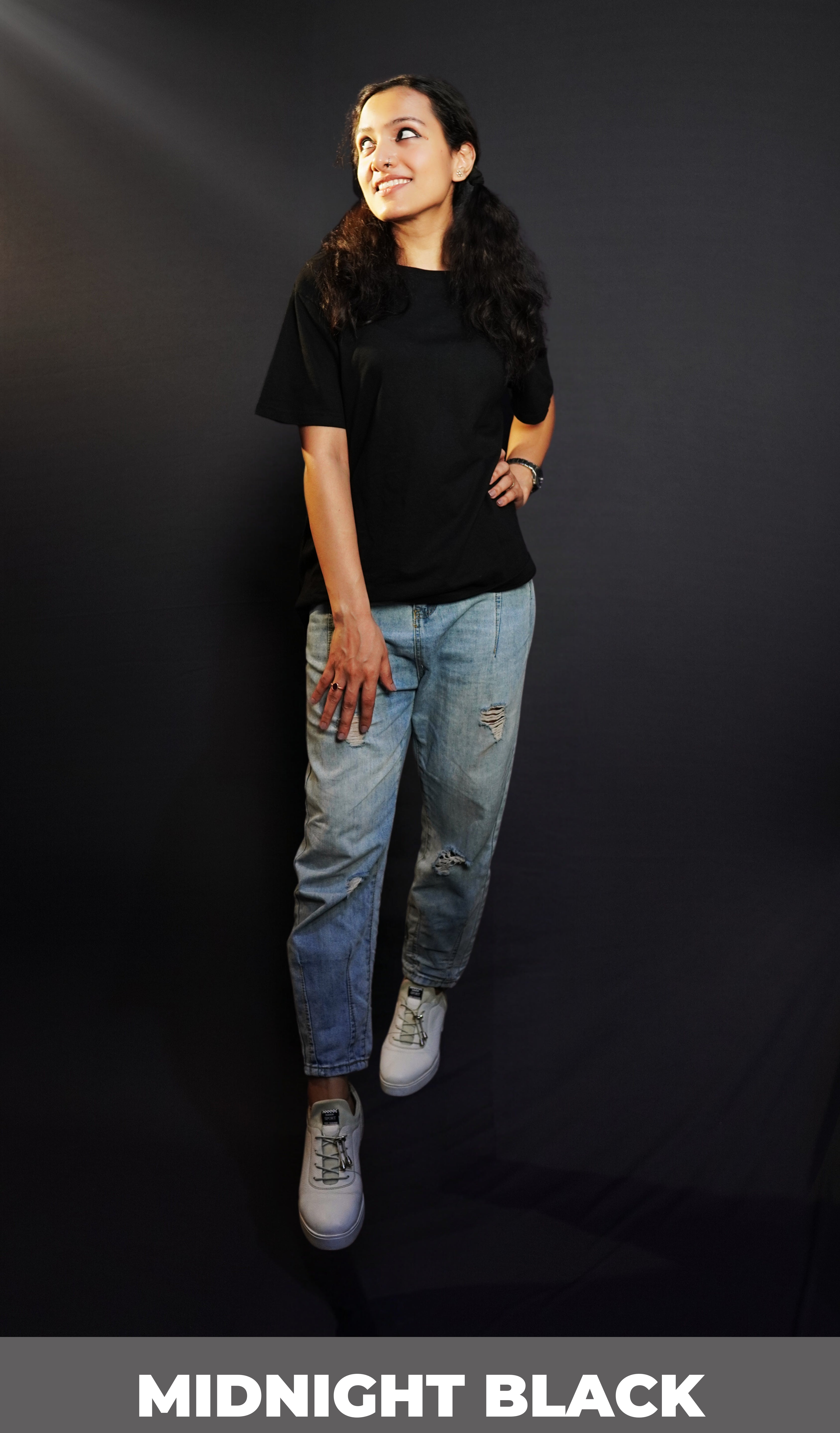 An elegant model wearing a short sleeved long length plain midnight black women's t-shirt, looking sideways as her hand gently lies on her waist and thigh, highlighting a stylish modern look-Muselot