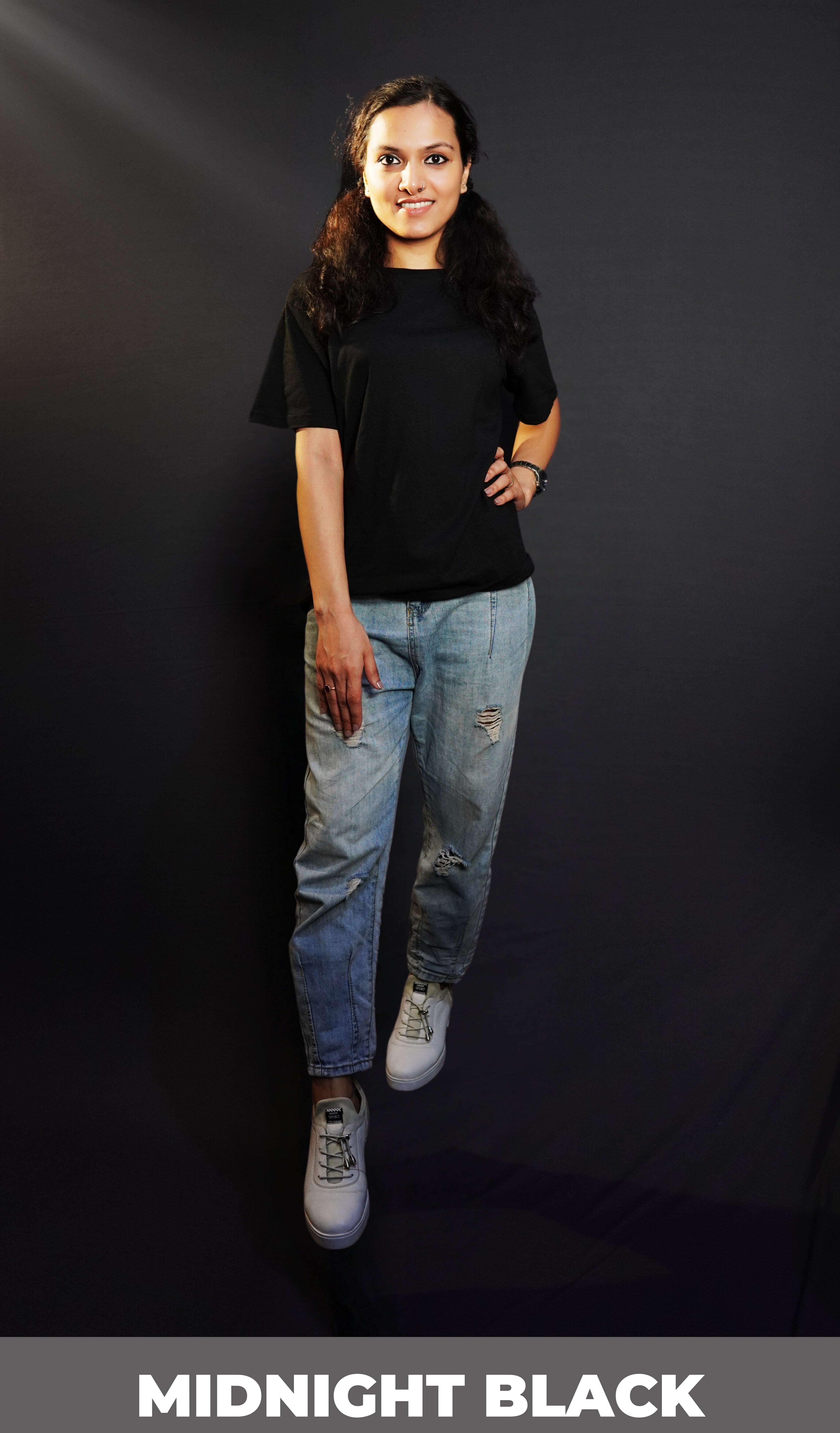 A classy model posing with her hand on her waist and another on her thigh looking directly at the camera, wearing a unisex quick drying summer midnight black stretchable t-shirt, highlighting an up to the minute in vague look-Muselot