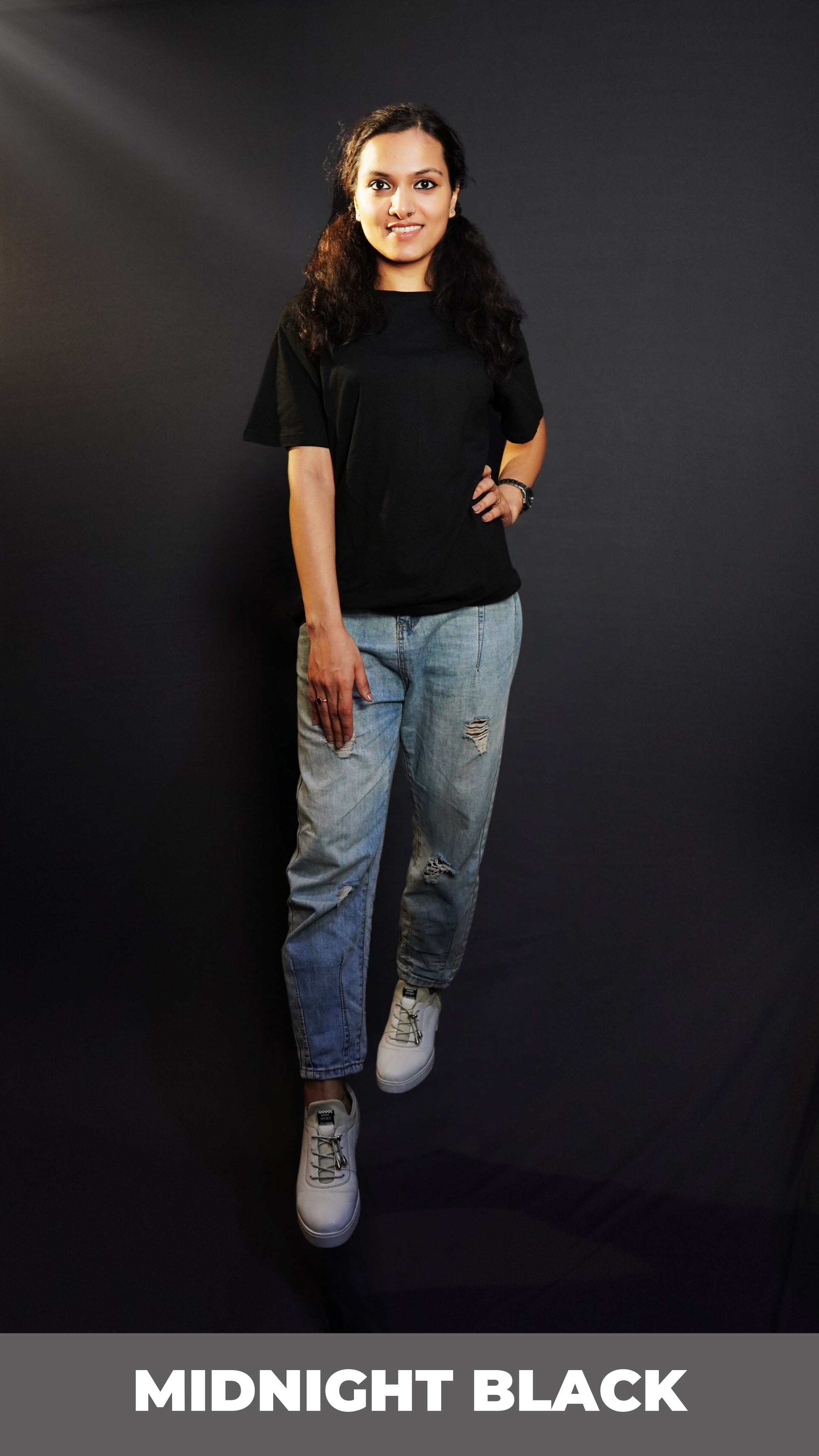 A classy model posing with her hand on her waist and another on her thigh looking directly at the camera, wearing a unisex quick drying summer midnight black stretchable t-shirt, highlighting an up to the minute in vague look-Muselot