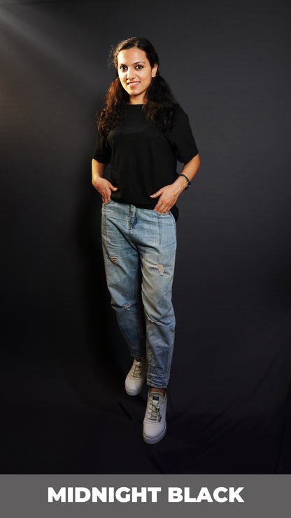 A model wearing a round neck cotton moisture wicking long length midnight black t-shirt, posing as her hands are slightly inside her jeans pockets, showcasing a classy trendy fit-Muselot