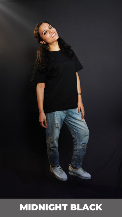 A woman posing happily with her slightly backwards and her gently resting on her thigh, wearing a plain short sleeved long length cotton midnight black t-shirt, showcasing an informal relaxed look-Muselot