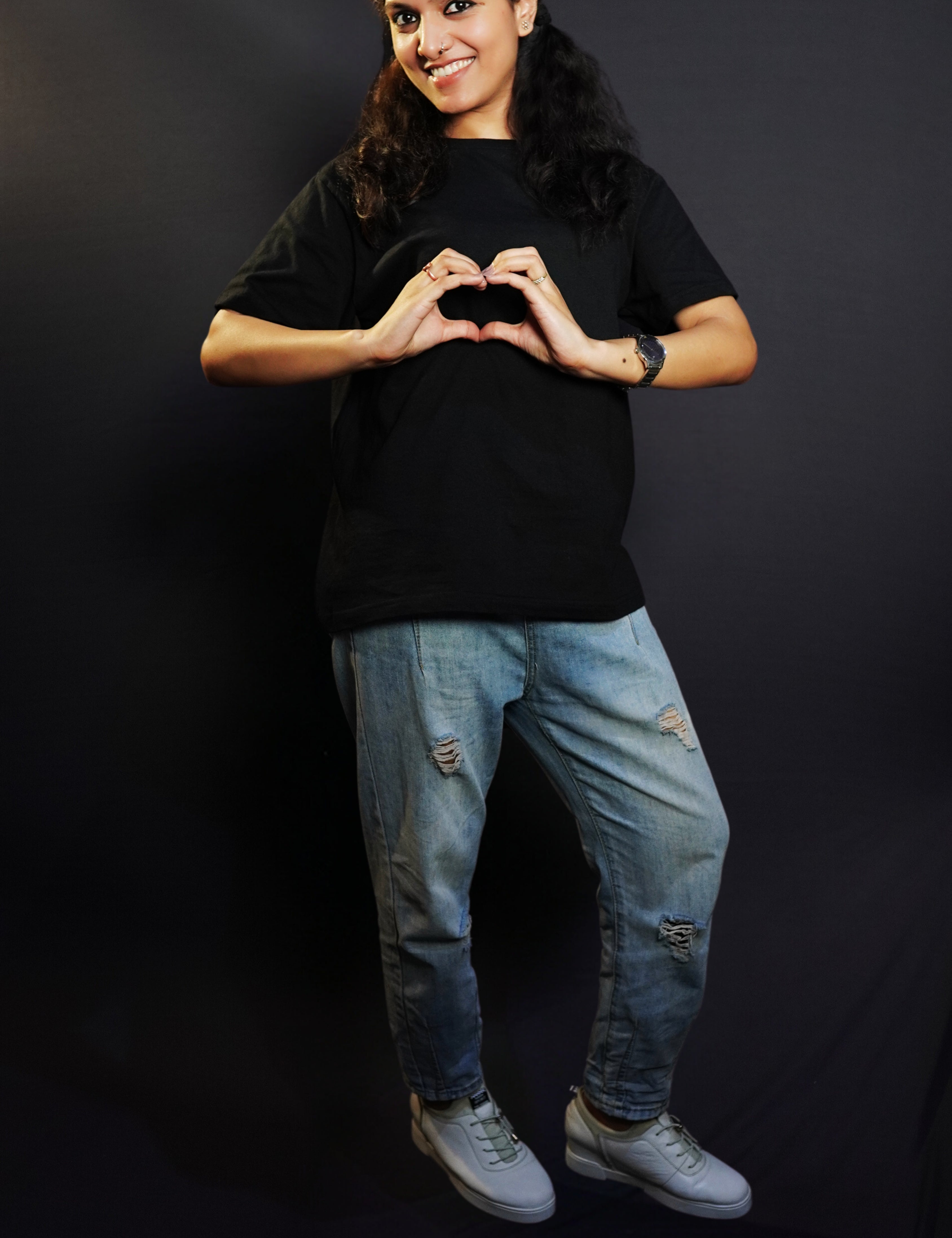 A woman posing happily with her hands making a heart smiling brightly, wearing a long length round neck quick drying stretchable cotton midnight black t-shirt, highlighting an in demand baggy fit-Muselot