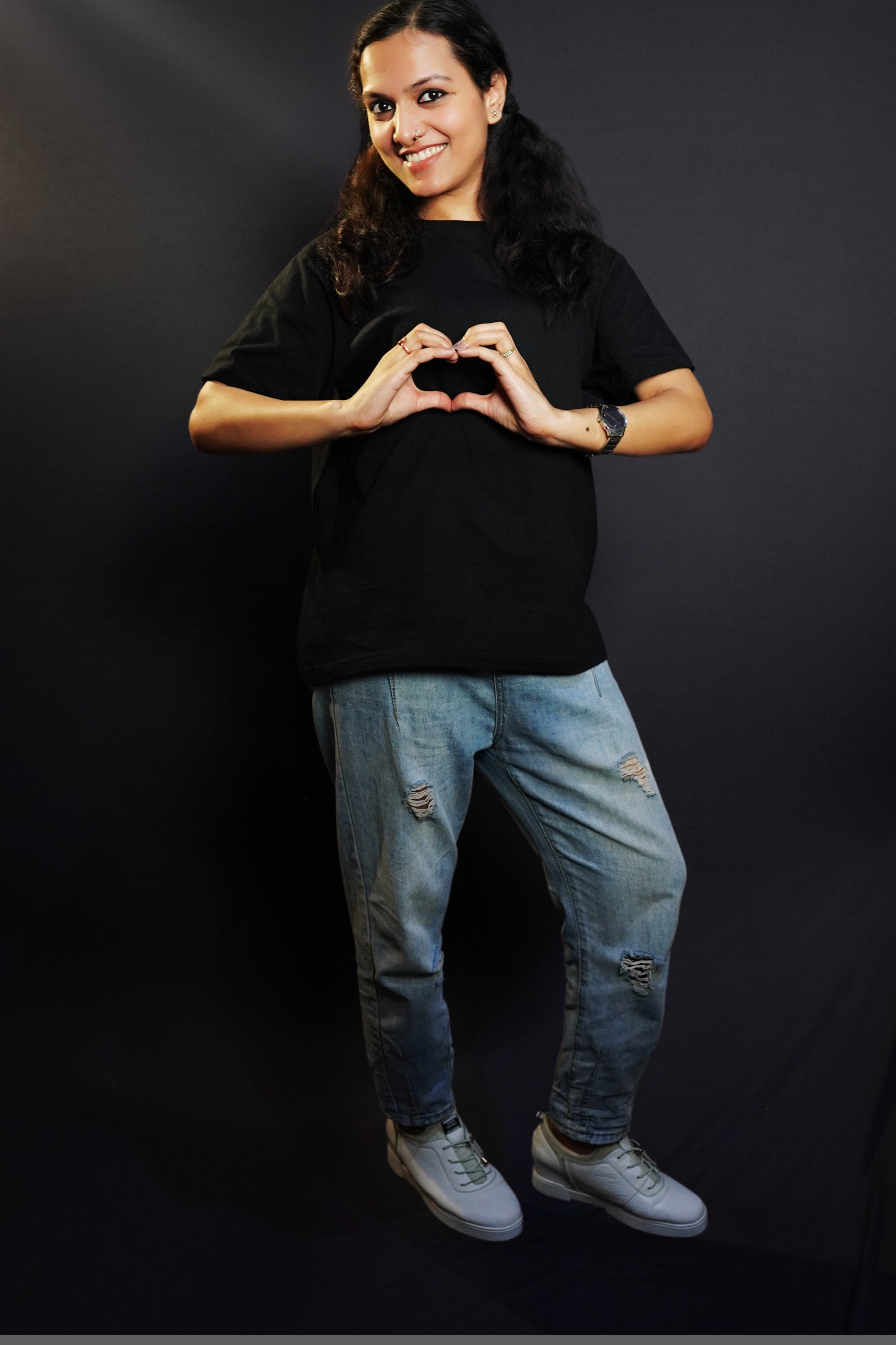 A woman posing happily with her hands making a heart smiling brightly, wearing a long length round neck quick drying stretchable cotton midnight black t-shirt, highlighting an in demand baggy fit-Muselot