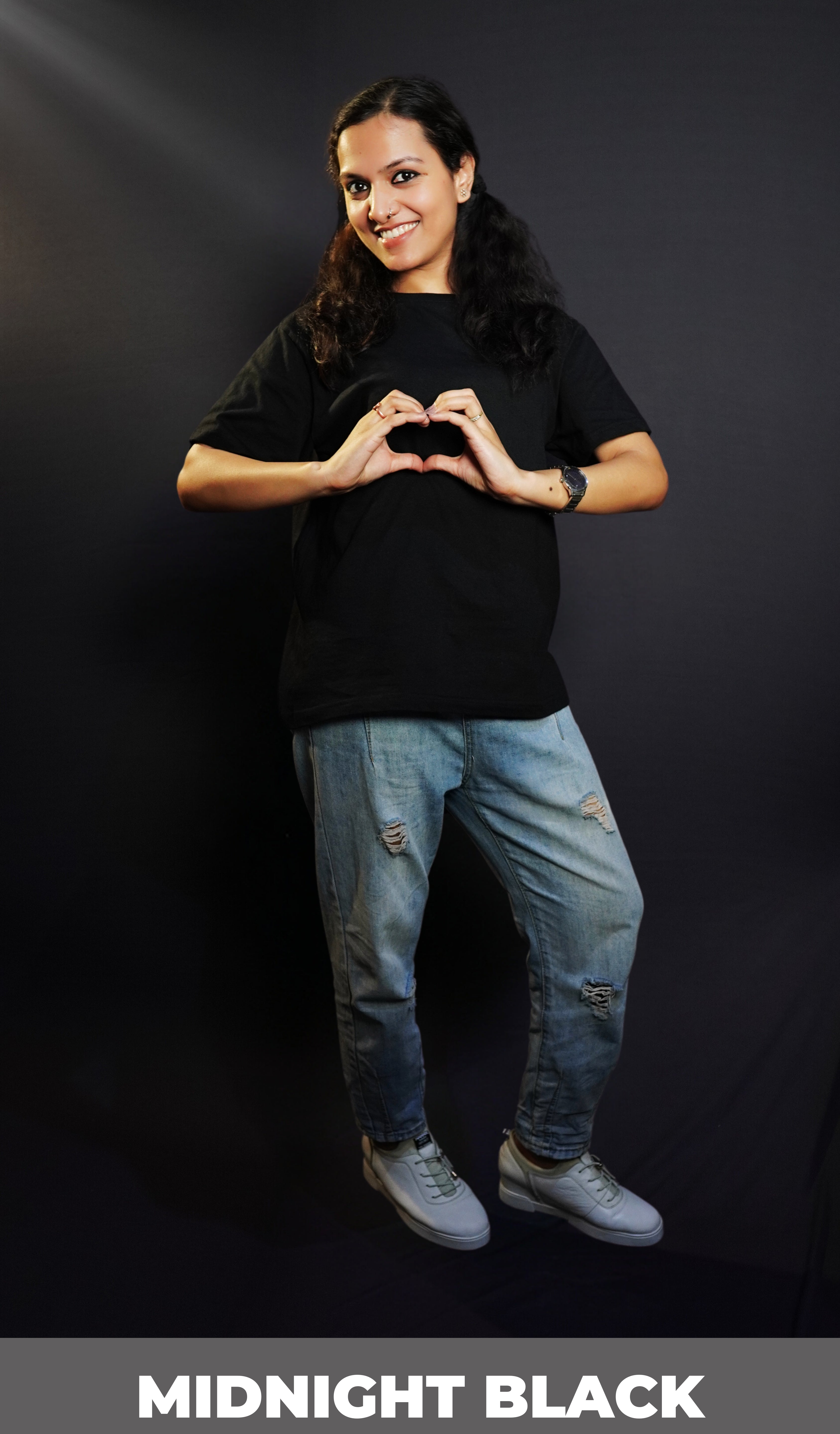 A woman posing happily with her hands making a heart smiling brightly, wearing a long length round neck quick drying stretchable cotton midnight black t-shirt, highlighting an in demand baggy fit-Muselot