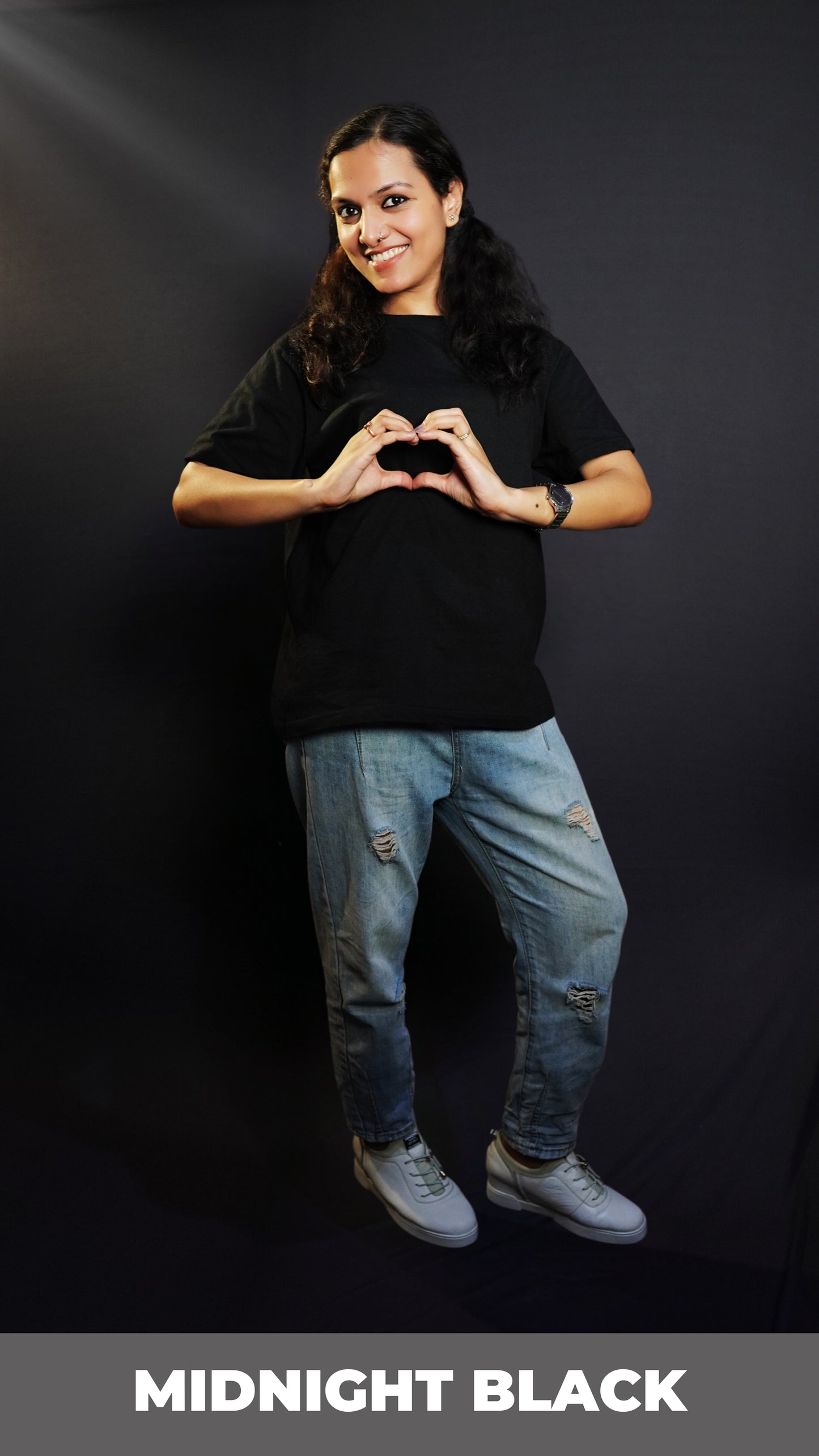 A woman posing happily with her hands making a heart smiling brightly, wearing a long length round neck quick drying stretchable cotton midnight black t-shirt, highlighting an in demand baggy fit-Muselot