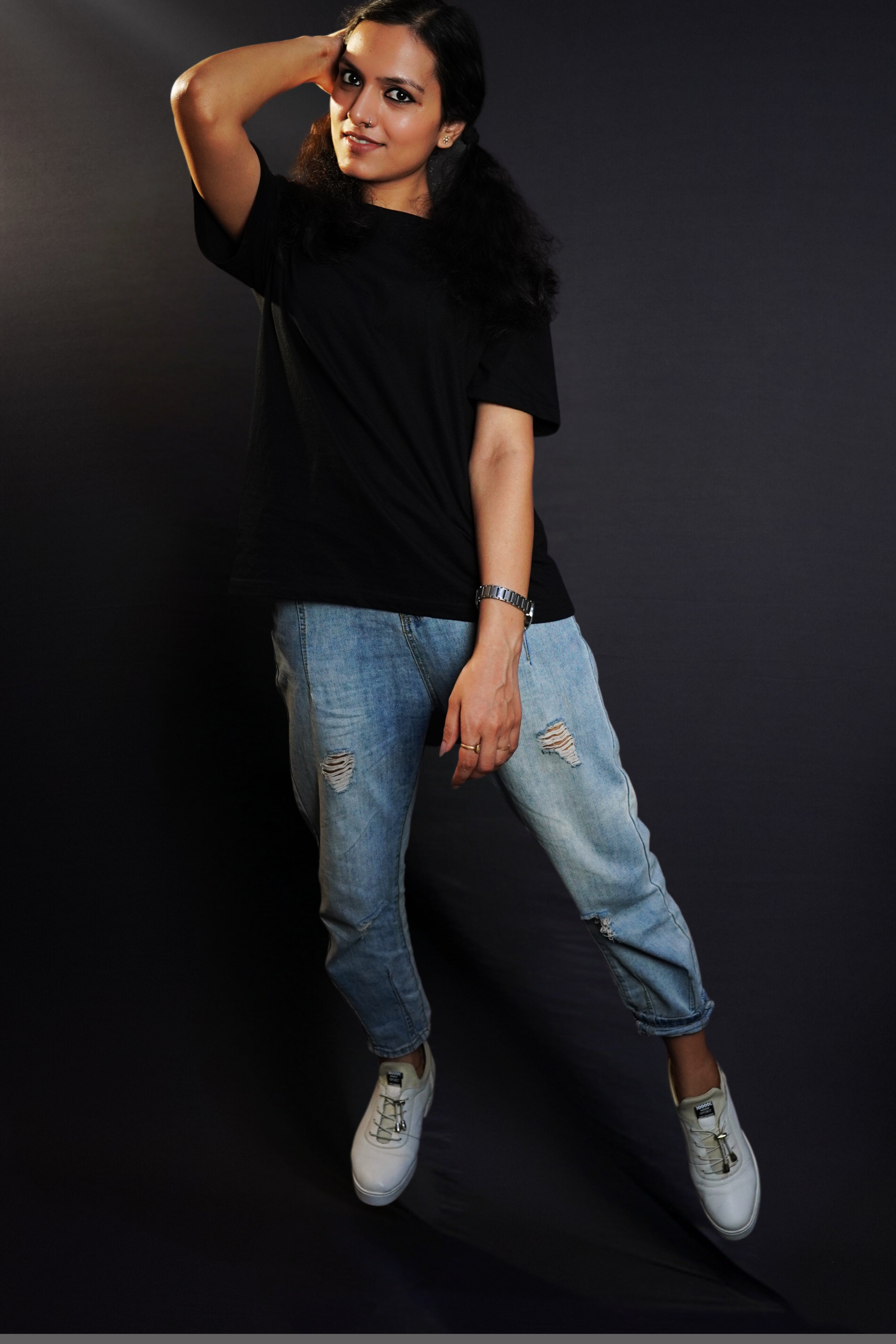 A stylish model wearing a plain short sleeved girl's cotton stretchable midnight black t-shirt, posing with her hand on the side of her head with elbow towards the camera, showcasing a fashionable snug fit-Muselot