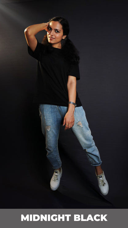 A stylish model wearing a plain short sleeved girl's cotton stretchable midnight black t-shirt, posing with her hand on the side of her head with elbow towards the camera, showcasing a fashionable snug fit-Muselot