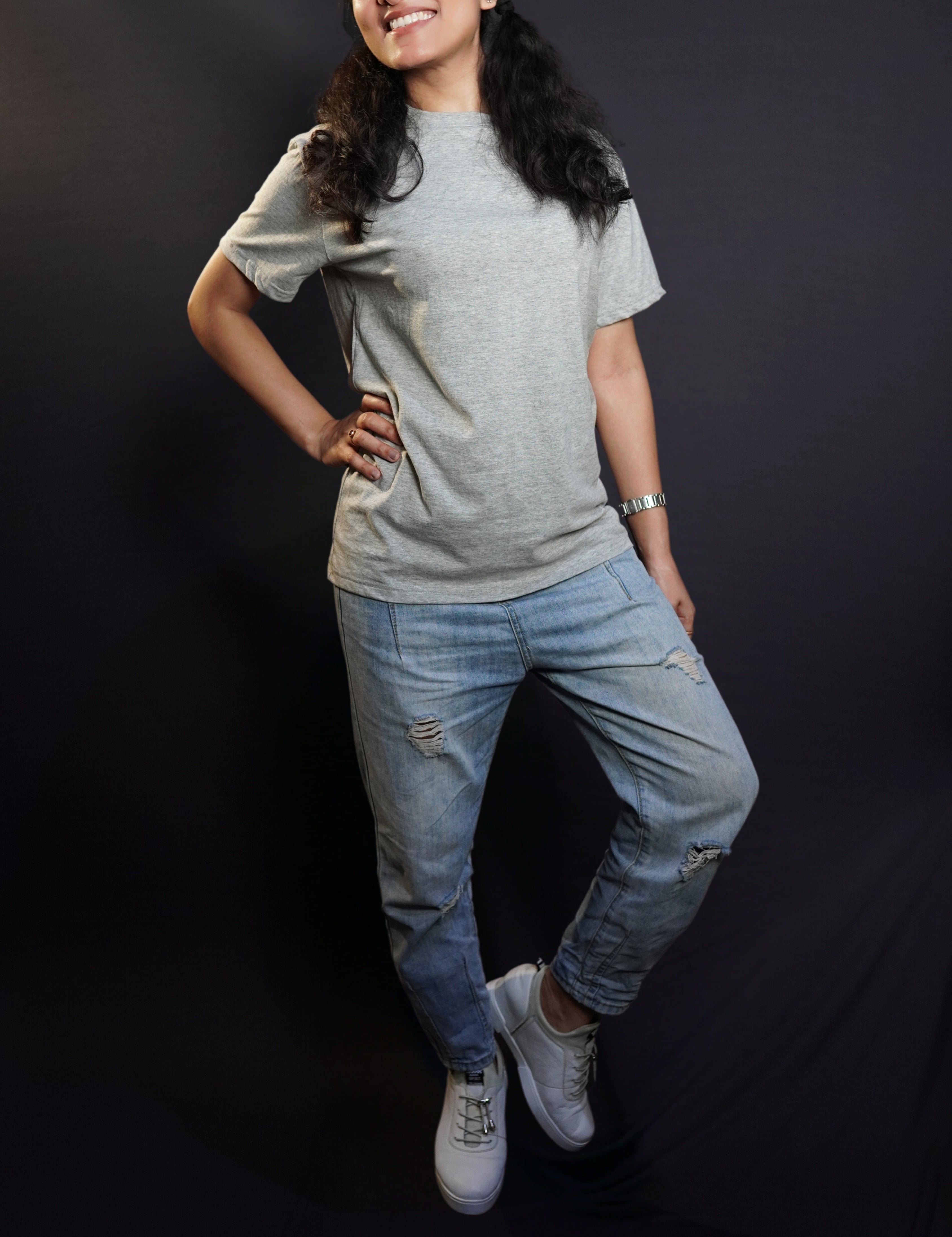 A happy woman posing with her hand on her waist and a leg bending on her side, wearing a men's plain long length misty grey t-shirt, showcasing a funky snug fit-Muselot
