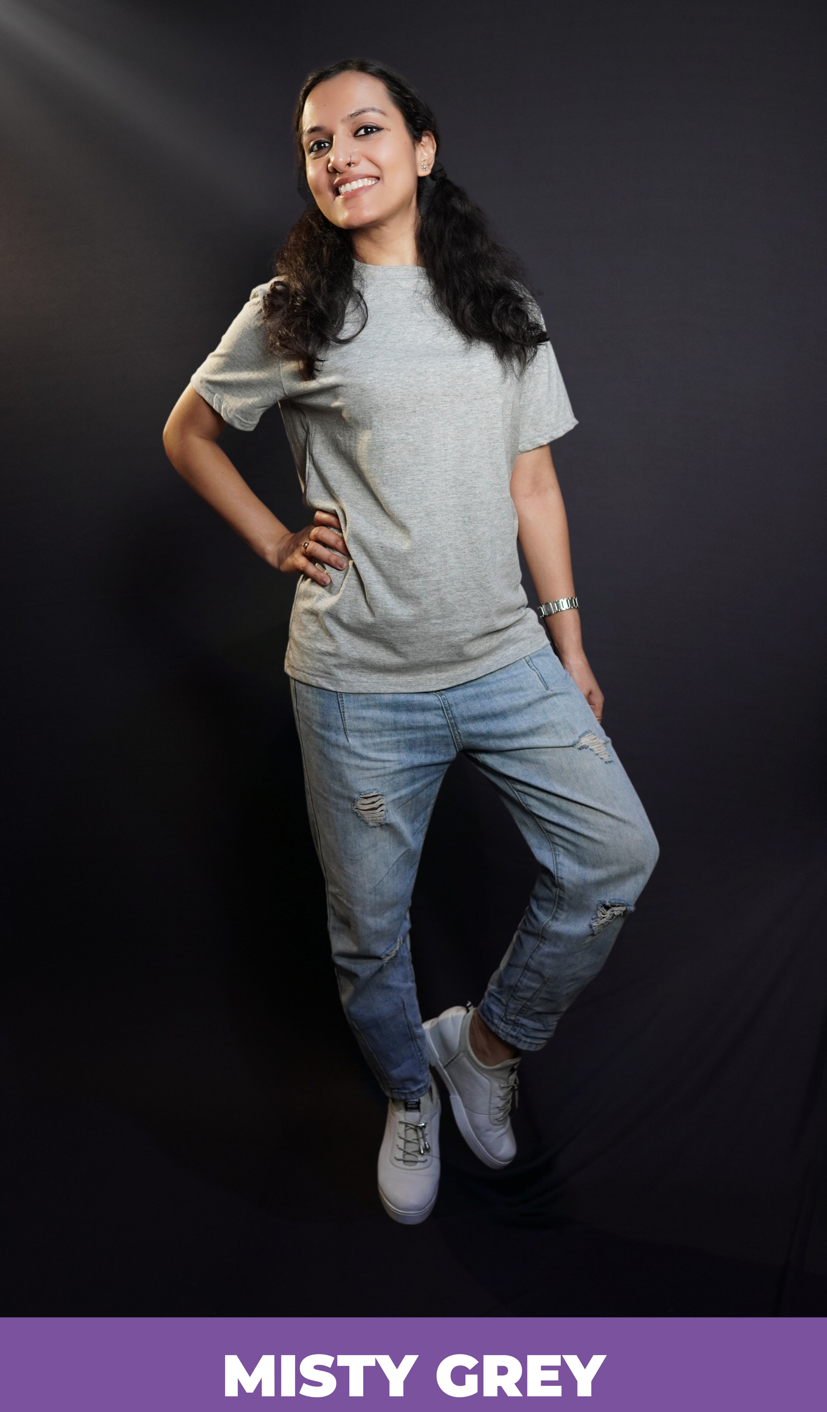 A happy woman posing with her hand on her waist and a leg bending on her side, wearing a men's plain long length misty grey t-shirt, showcasing a funky snug fit-Muselot
