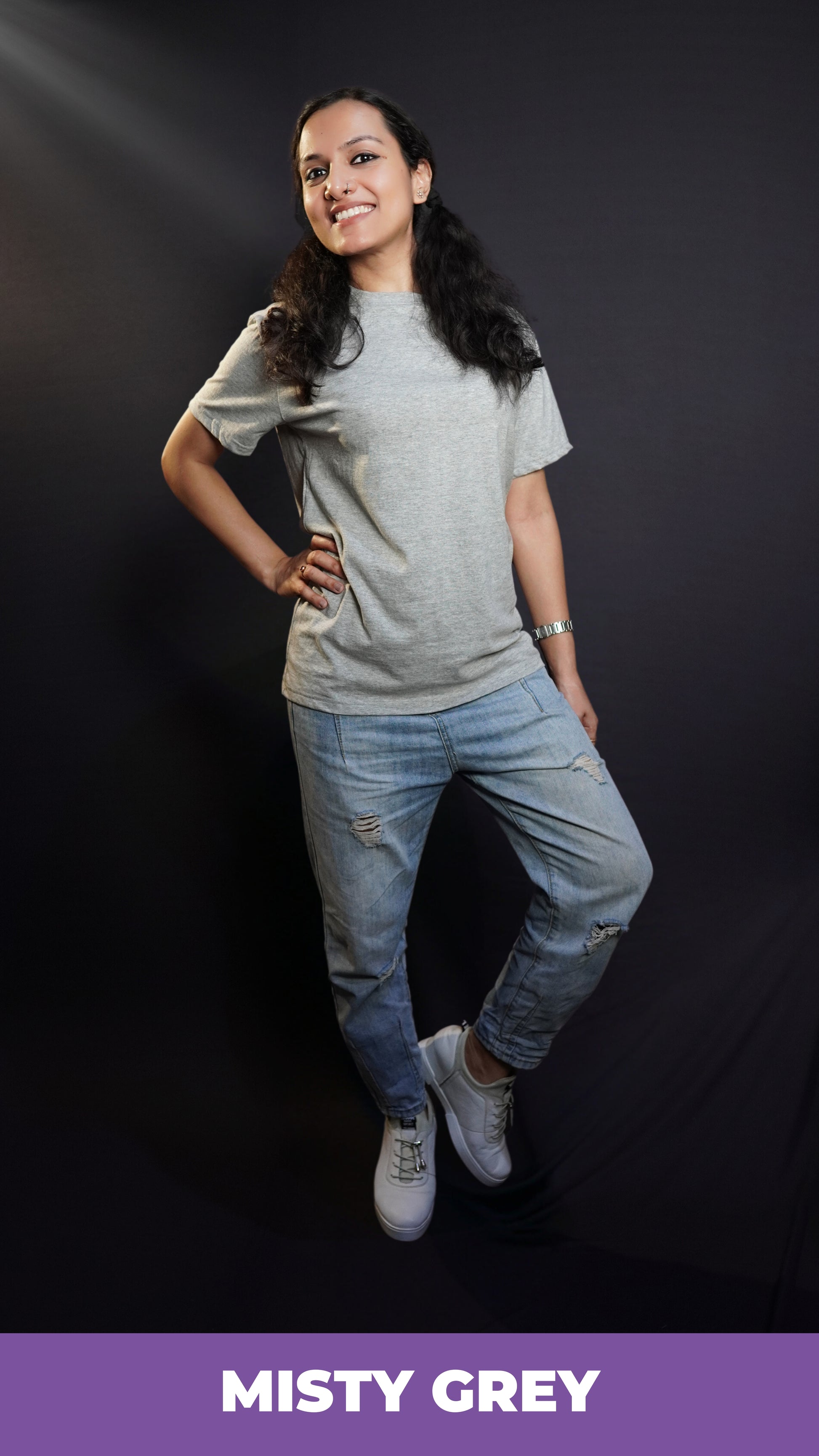 A happy woman posing with her hand on her waist and a leg bending on her side, wearing a men's plain long length misty grey t-shirt, showcasing a funky snug fit-Muselot