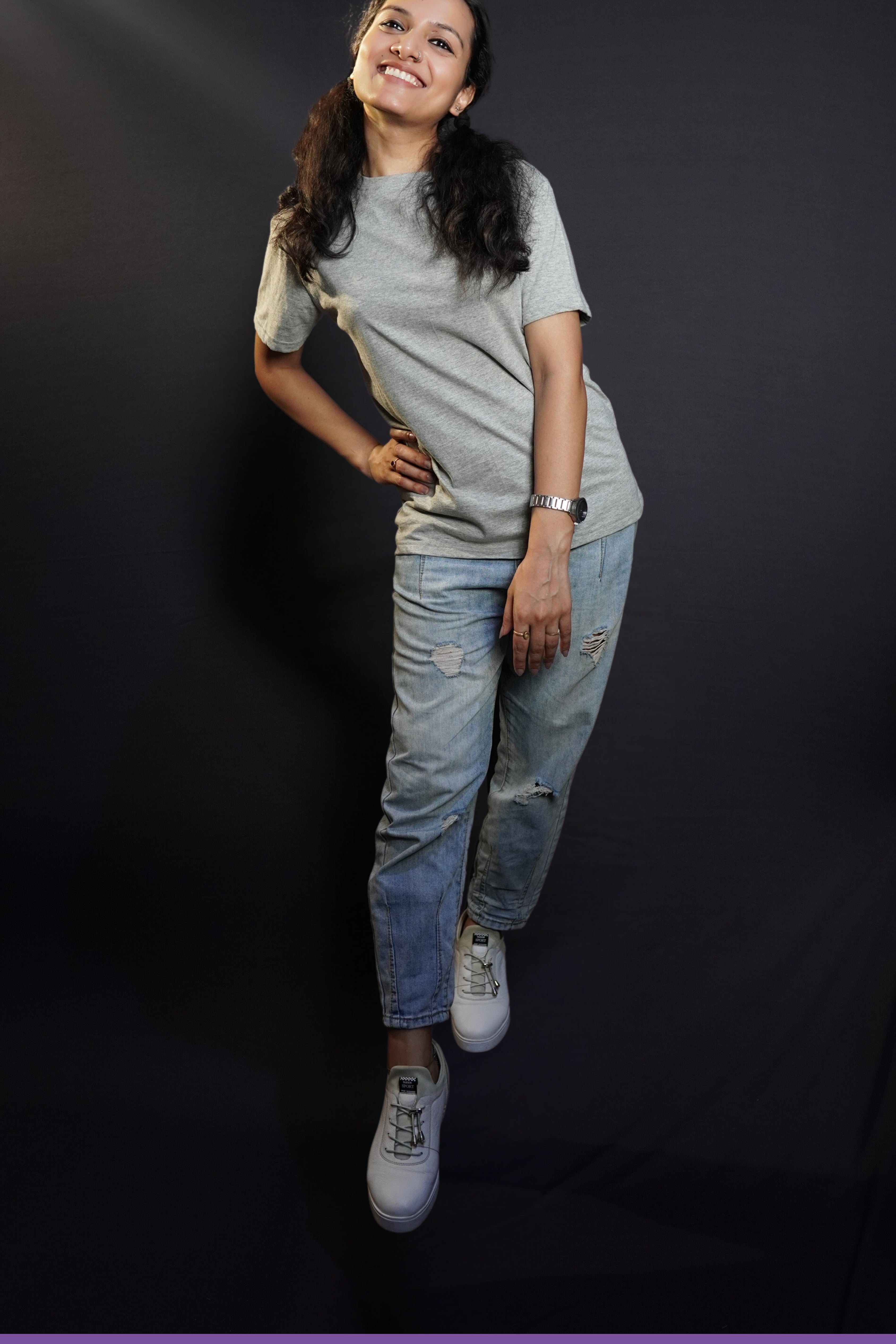A cute woman wearing adult's round neck long length short sleeved misty grey t-shirt, posing with her hand on her waist as she sways to her side, highlighting a up to the minute easygoing fit-Muselot