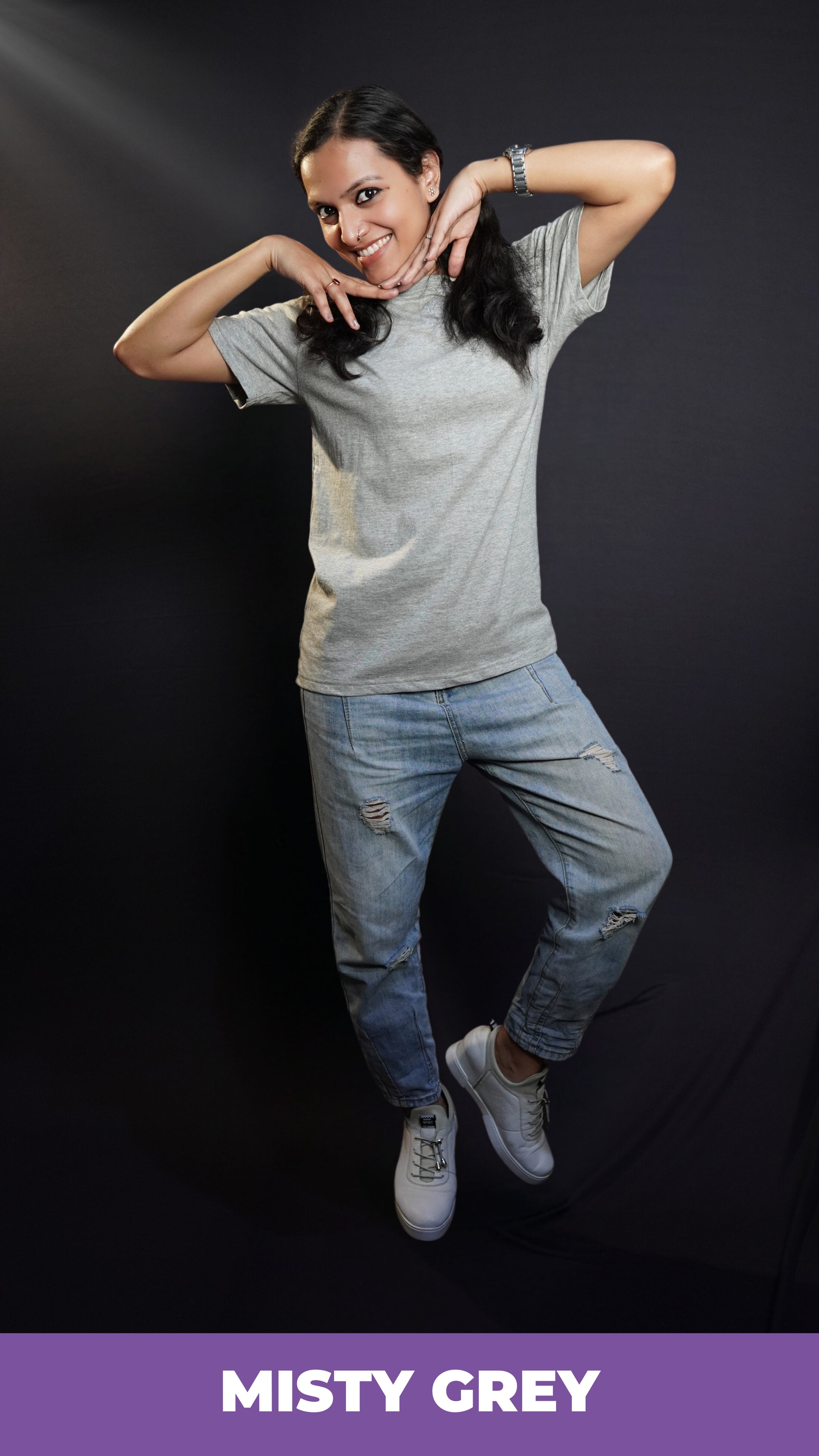 A woman posing happily with her hands under her chin, wearing a plain stretchable quick drying round neck misty grey plain t-shirt, highlighting a relaxed fashionable look-Muselot