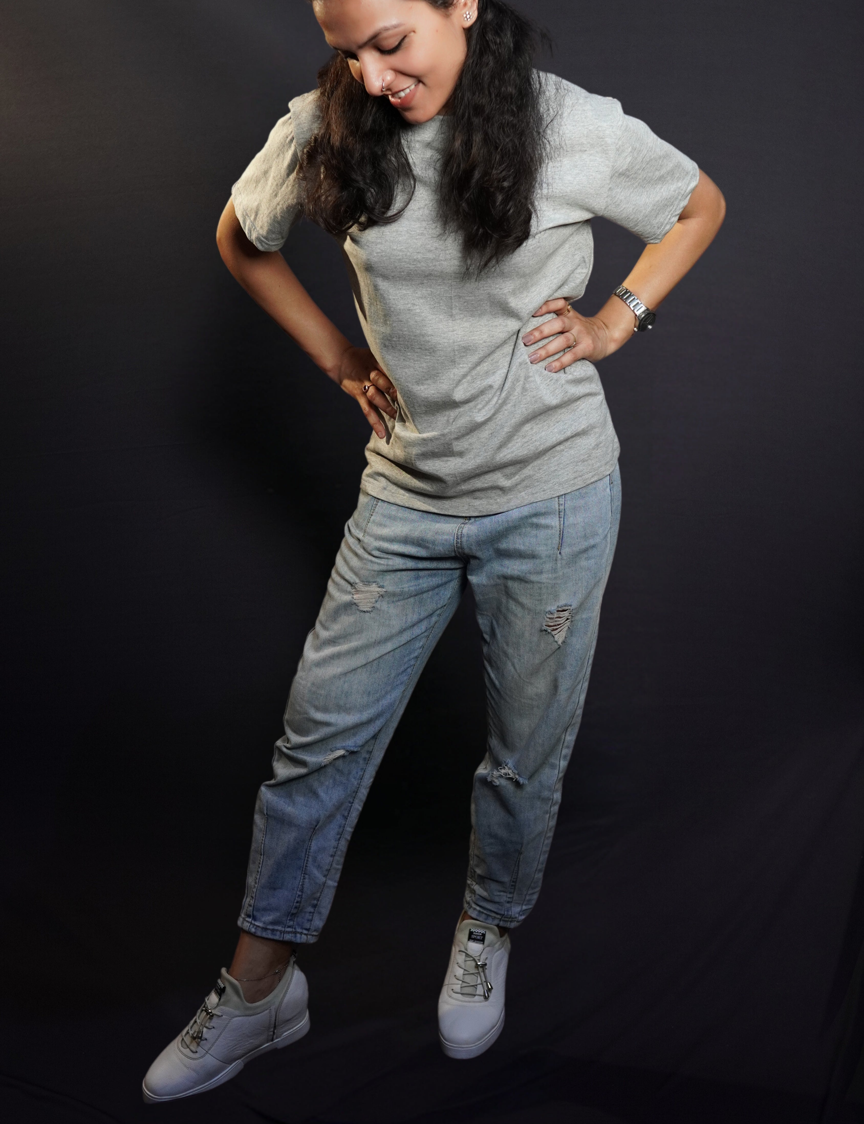 A woman posing with her hands on her waist standing slghtly sideways bending down a little, wearing a plain unisex short sleeved stretchable misty grey t-shirt, highlighting a stylish comfortable fit-Muselot