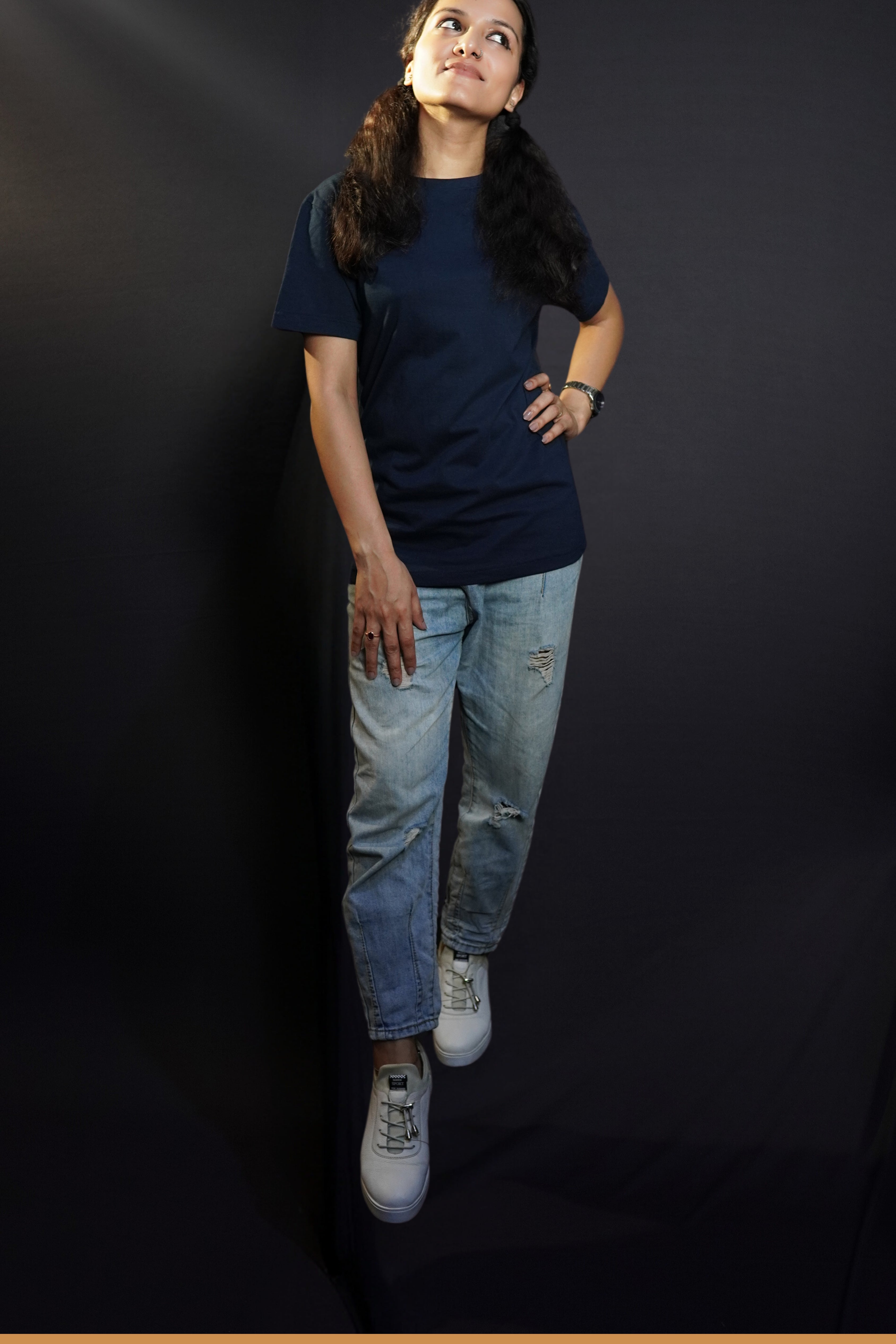 An elegant model wearing a women's cotton round neck stretchable plain navy blue t-shirt, posing with her hand on her waist and other on her thigh as she looks sideways with her chin up high, showcasing a popular modish look-Muselot