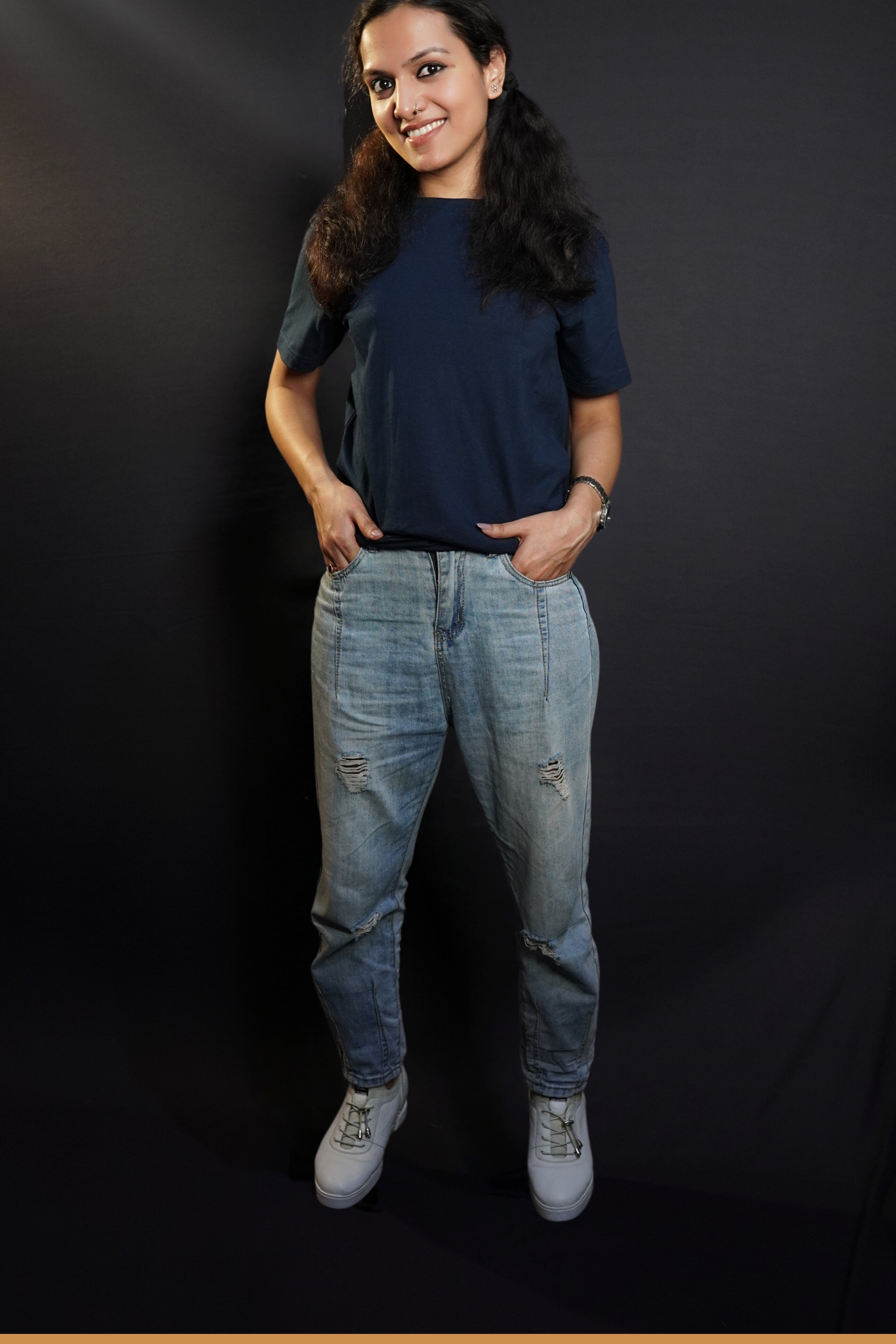 A woman wearing a men's summer short sleeved plain navy blue t-shirt, posing with her fingers inside the pockets of her jeans, highlighting a modish in vague fit-Muselot