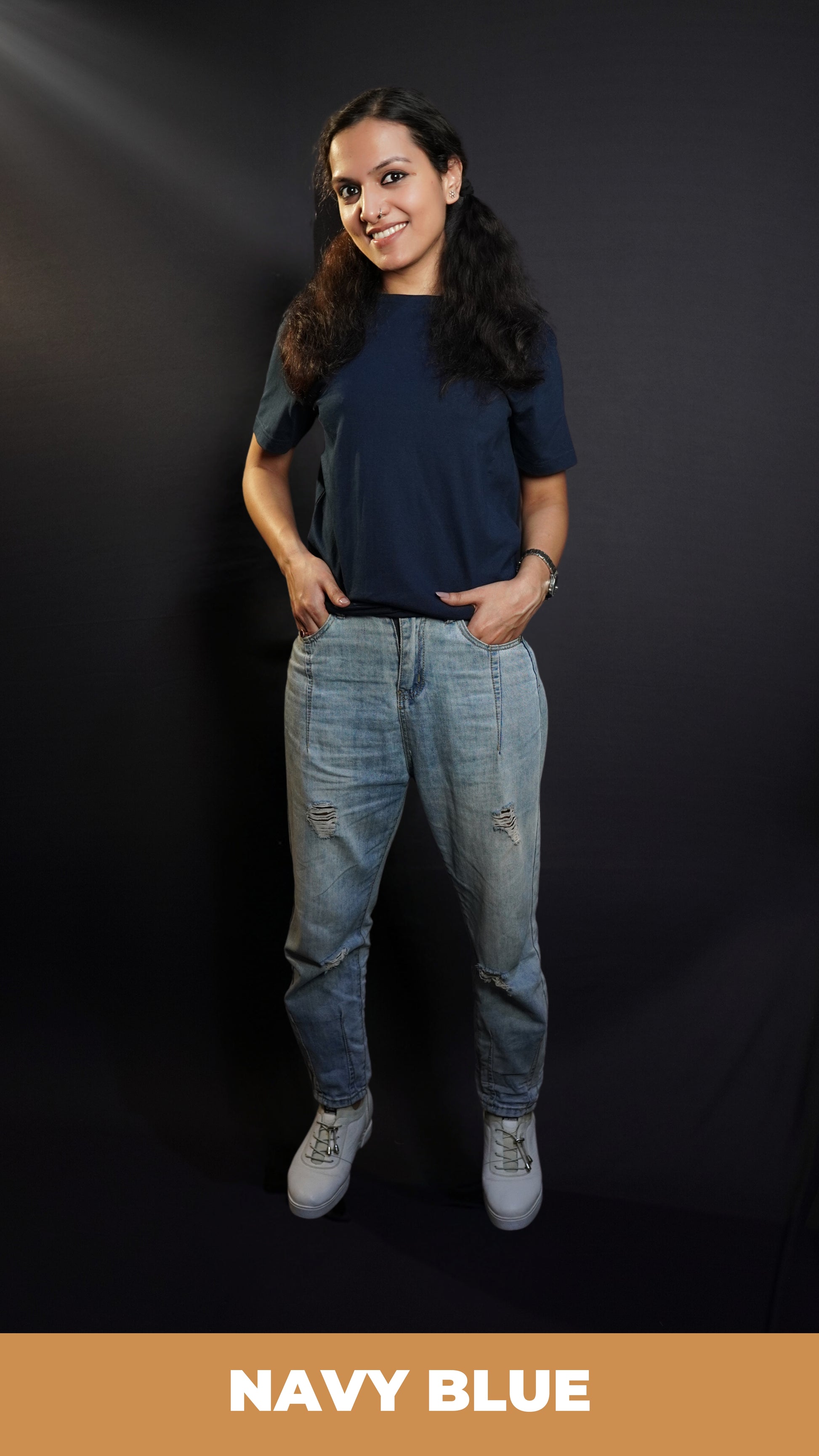 A woman wearing a men's summer short sleeved plain navy blue t-shirt, posing with her fingers inside the pockets of her jeans, highlighting a modish in vague fit-Muselot