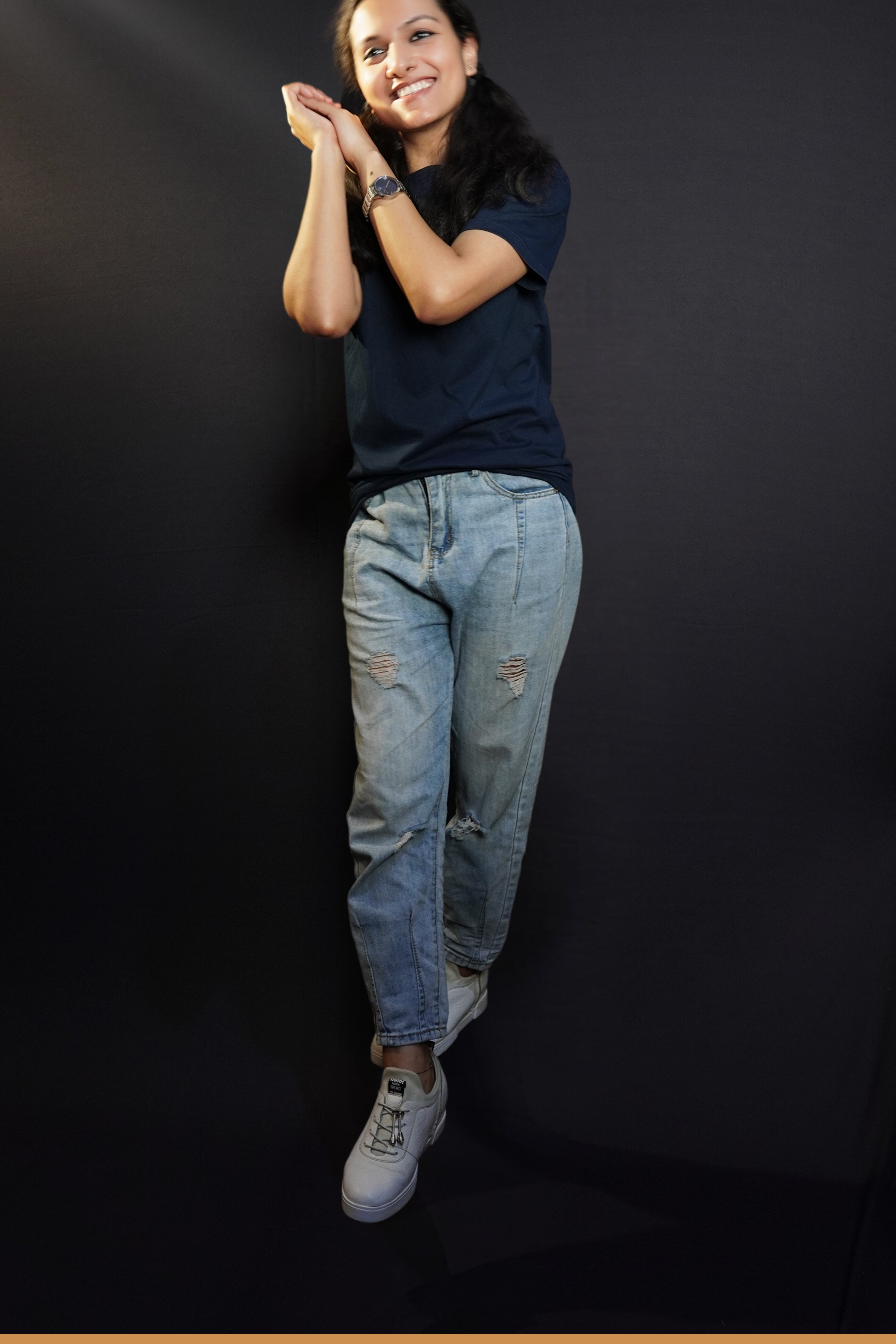 A woman wearing a cotton round neck short sleeved moisture wicking navy blue t-shirt, posing with her palms hugging each other near her head, showcasing a modish in vague look-Muselot