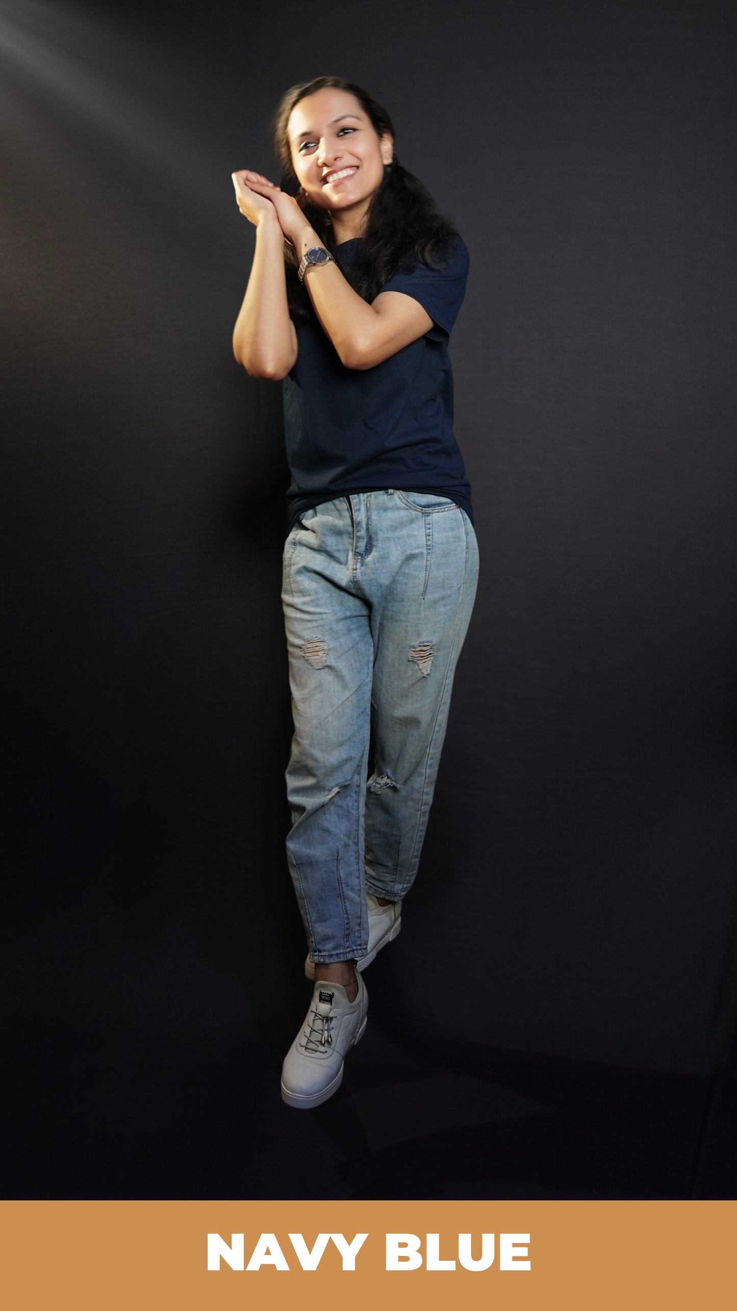 A woman wearing a cotton round neck short sleeved moisture wicking navy blue t-shirt, posing with her palms hugging each other near her head, showcasing a modish in vague look-Muselot