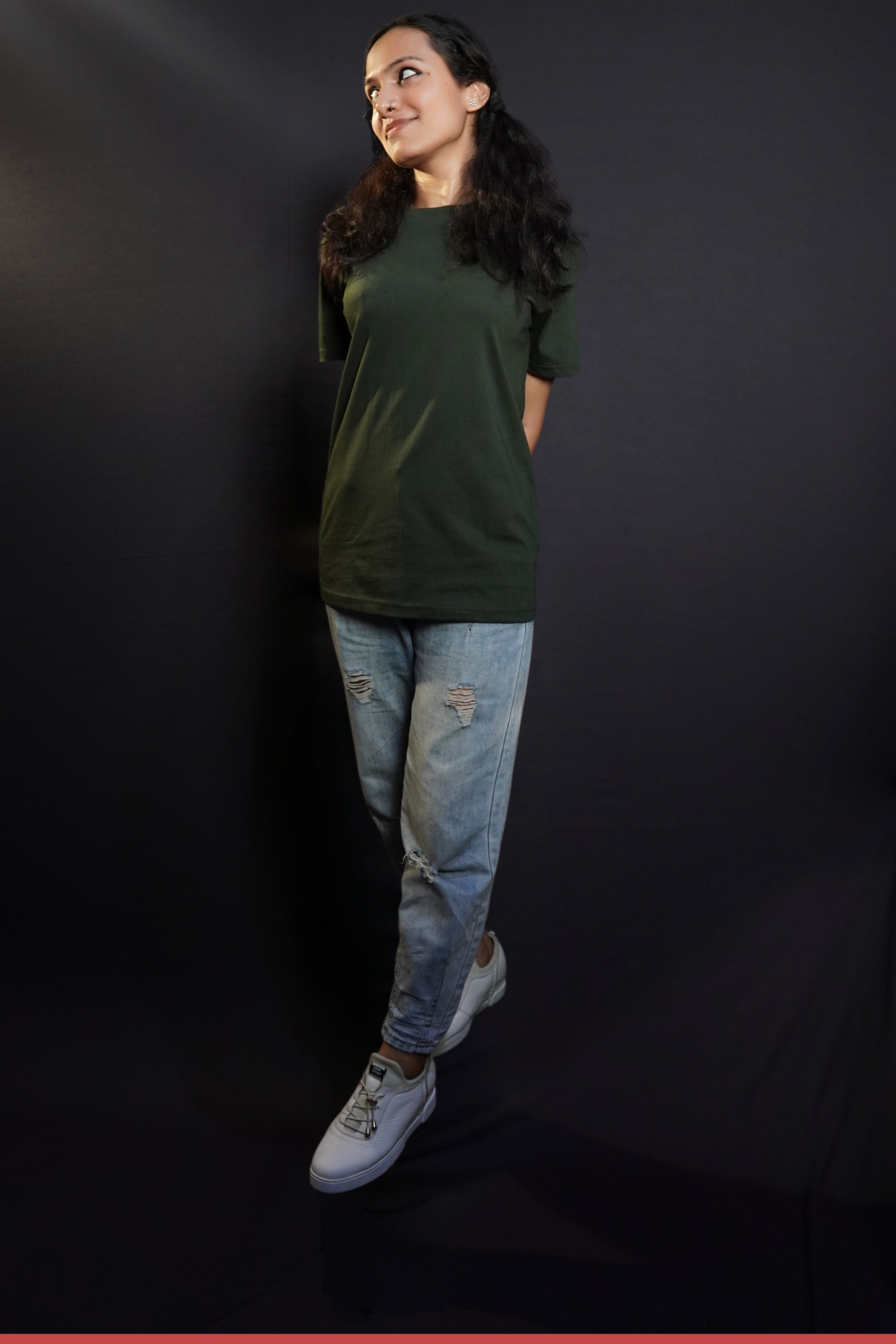 A stylish model posing with her hands at her back as she walks against a dark background, wearing a unisex plain round neck olive green t-shirt, showcasing a trendy snug fit-Muselot