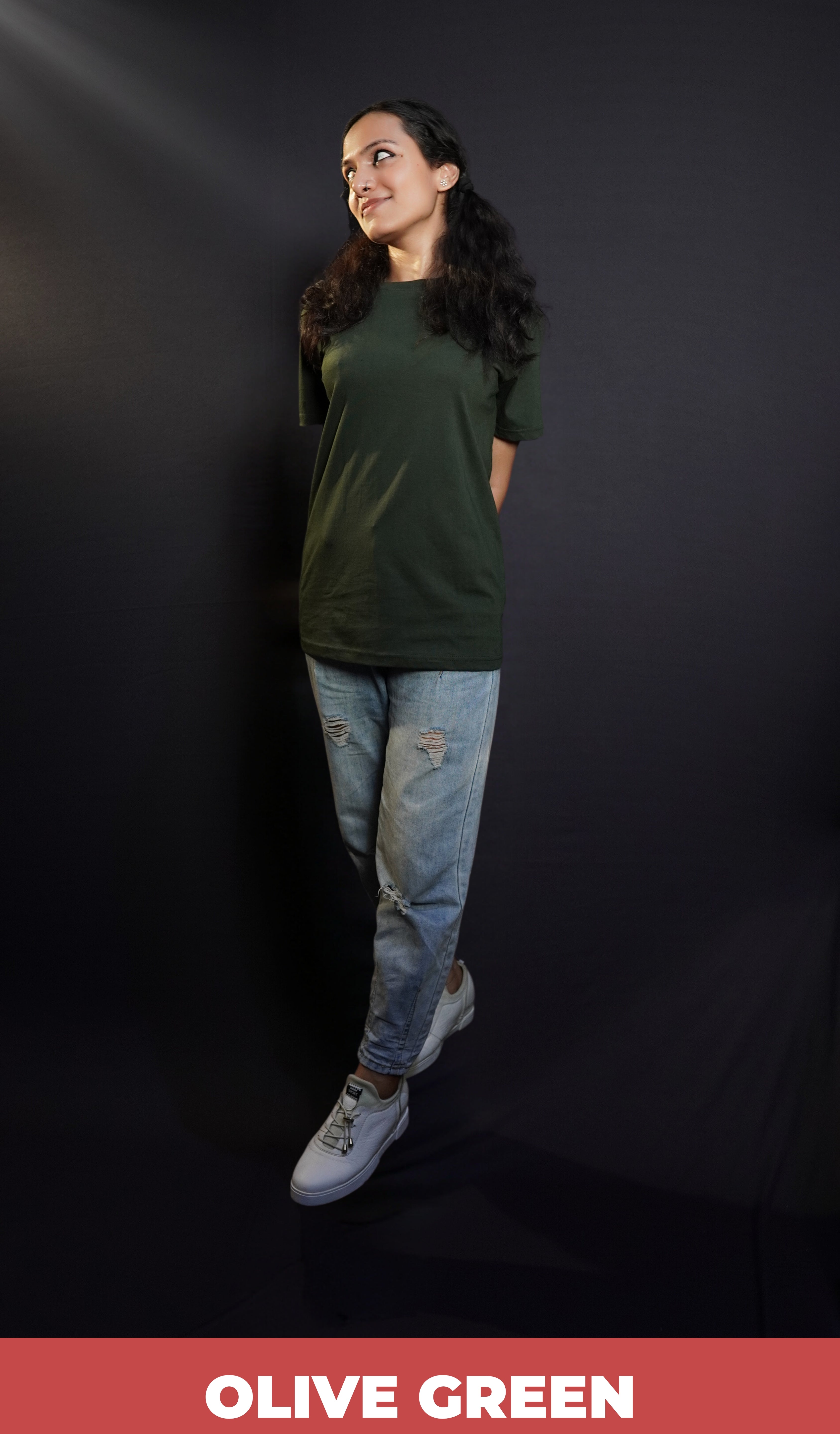 A stylish model posing with her hands at her back as she walks against a dark background, wearing a unisex plain round neck olive green t-shirt, showcasing a trendy snug fit-Muselot