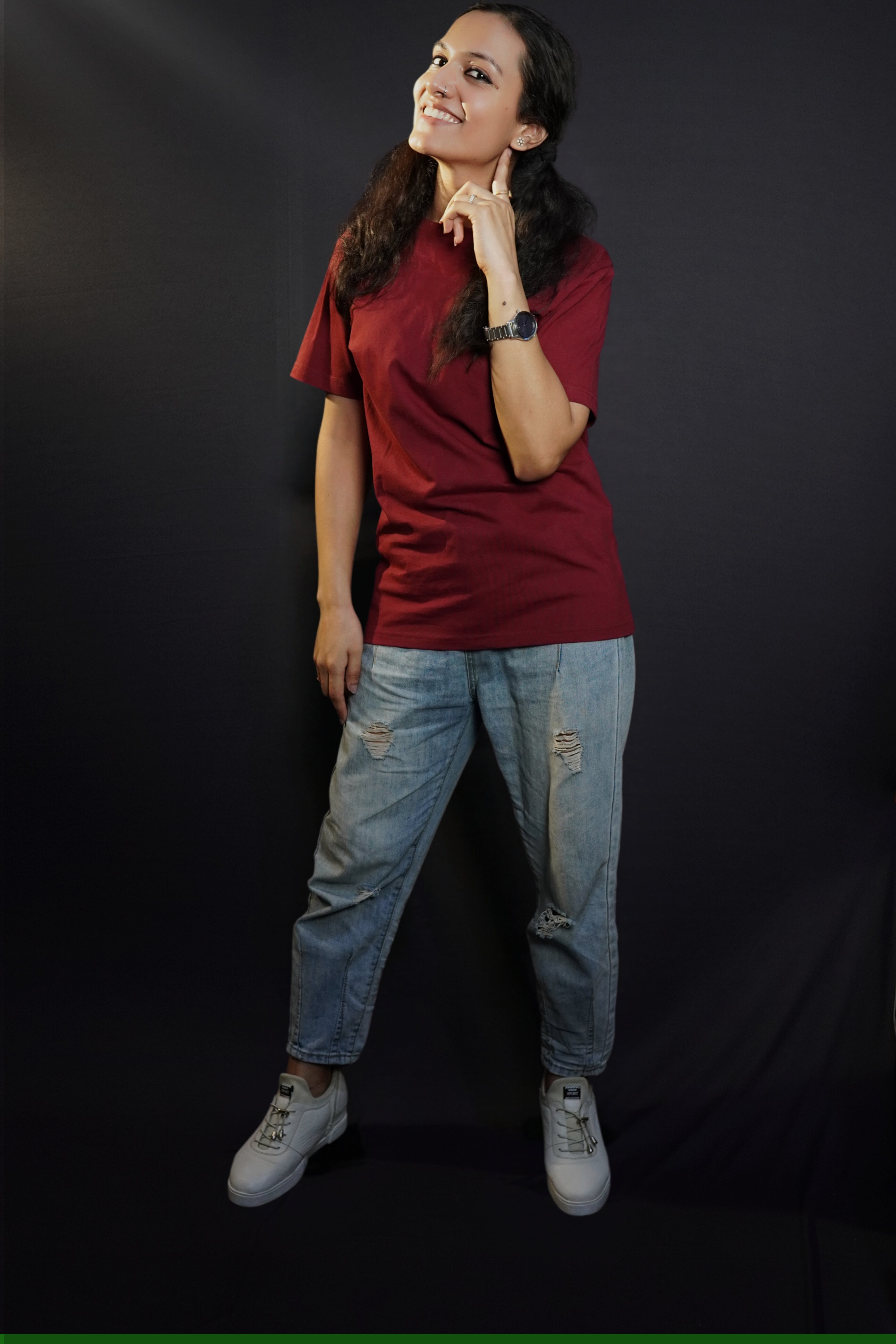 A woman wearing a girl's round neck stretchable rich maroon t-shirt, posing with her finger under her ear and other hanging on her side, showcasing a cool cozy look-Muselot