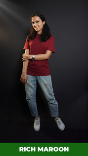 A woman wearing a plus size short sleeved moisture wicking rich maroon t-shirt, posing with her hand grabbing her elbow, smiling happily, highlighting a popular baggy fit-Muselot