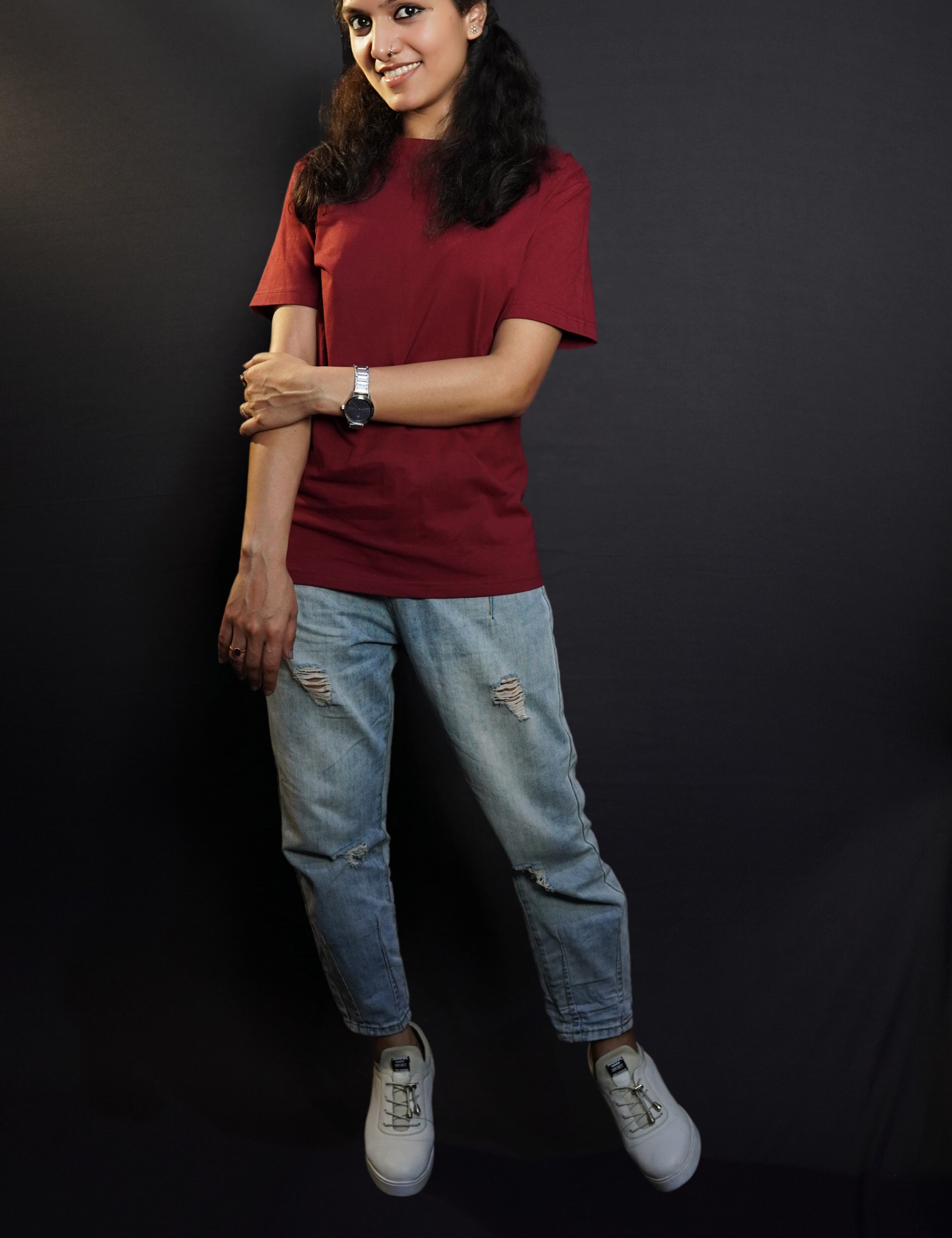 A woman wearing a plus size short sleeved moisture wicking rich maroon t-shirt, posing with her hand grabbing her elbow, smiling happily, highlighting a popular baggy fit-Muselot