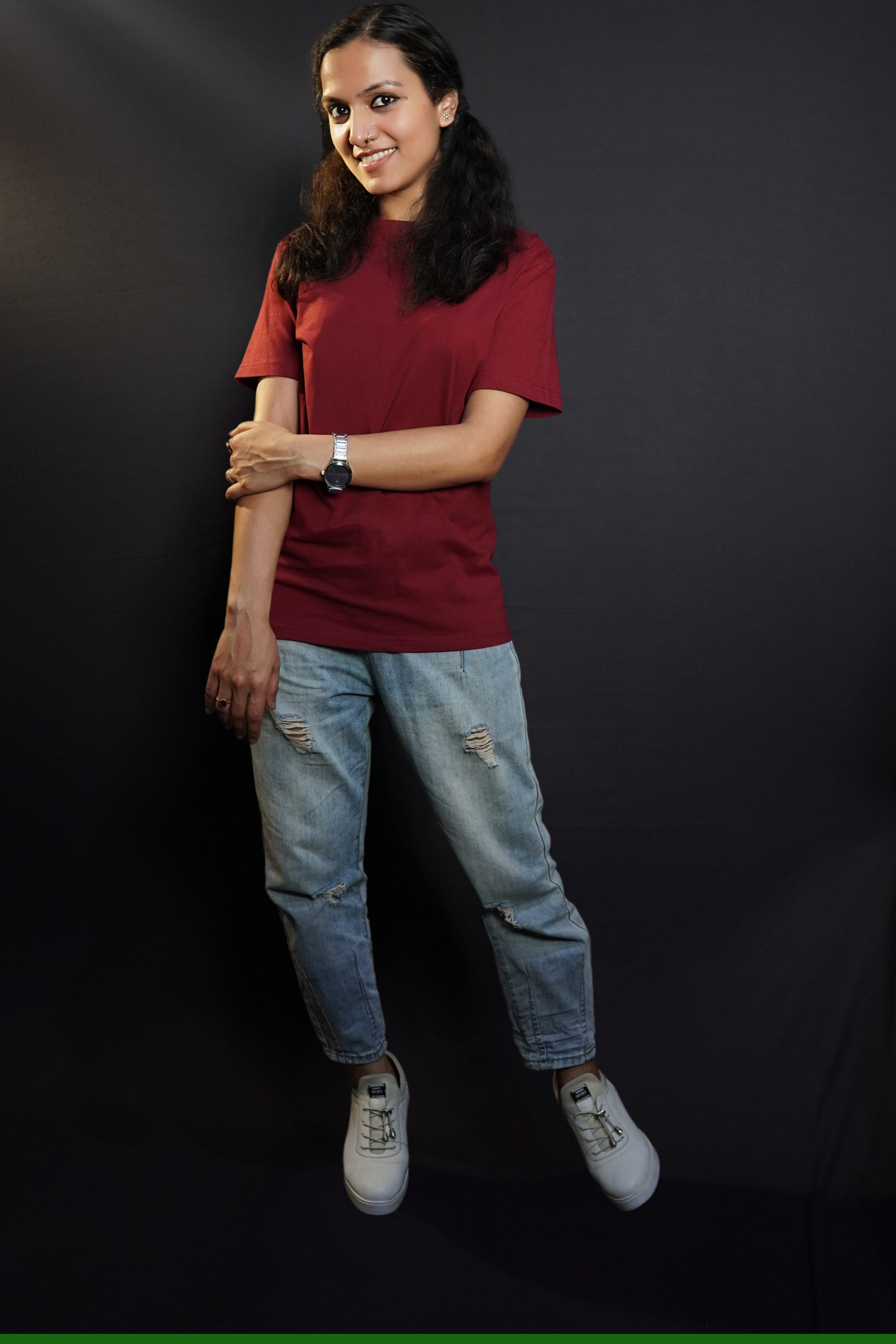 A woman wearing a plus size short sleeved moisture wicking rich maroon t-shirt, posing with her hand grabbing her elbow, smiling happily, highlighting a popular baggy fit-Muselot