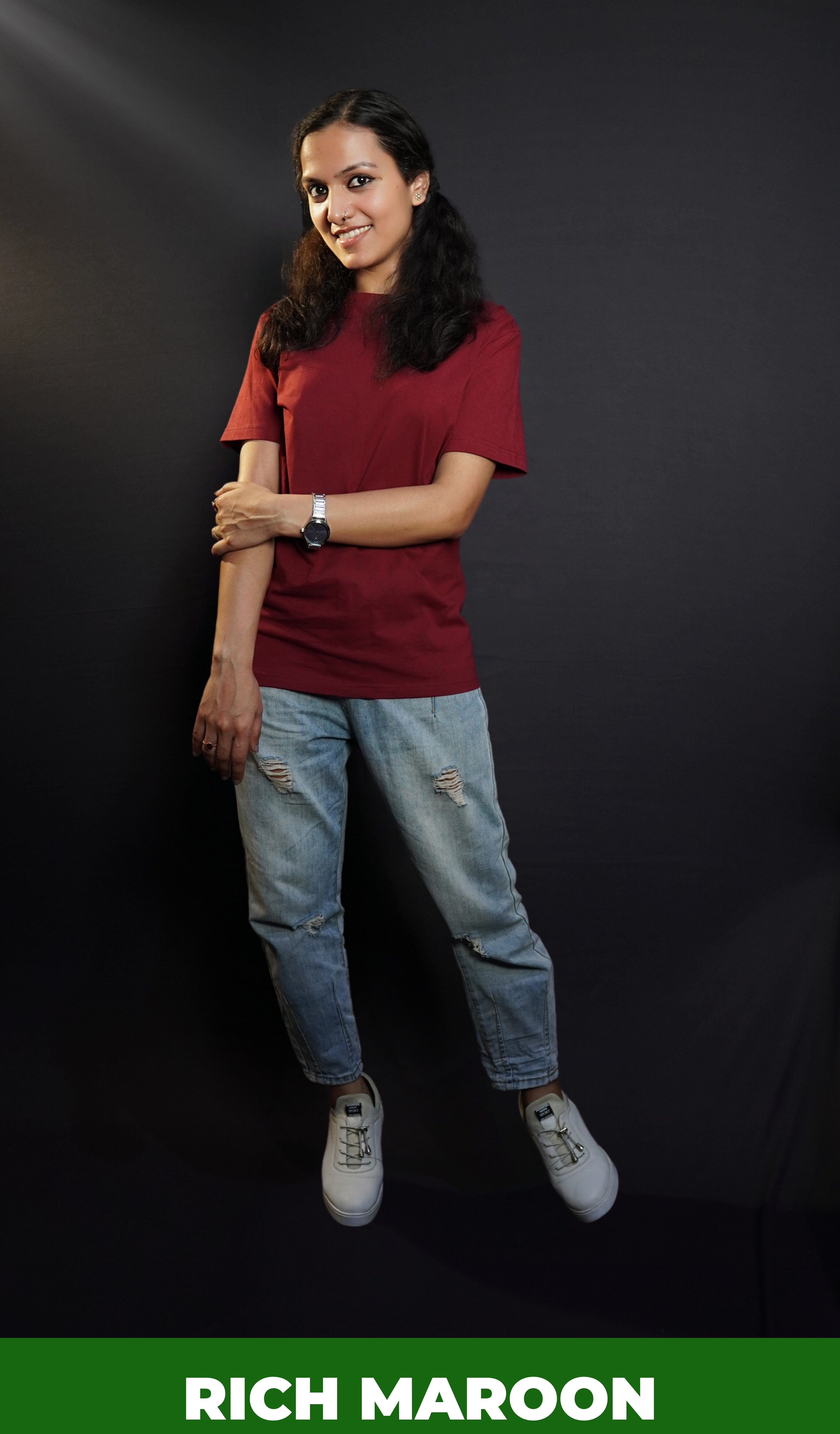 A woman wearing a plus size short sleeved moisture wicking rich maroon t-shirt, posing with her hand grabbing her elbow, smiling happily, highlighting a popular baggy fit-Muselot