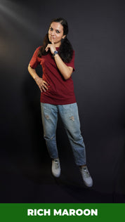 A woman wearing a round neck plain moisture wicking rich maroon t-shirt, posing with her finger on her lips and hand on her waist, highlighting a swank up to the minute look-Muselot