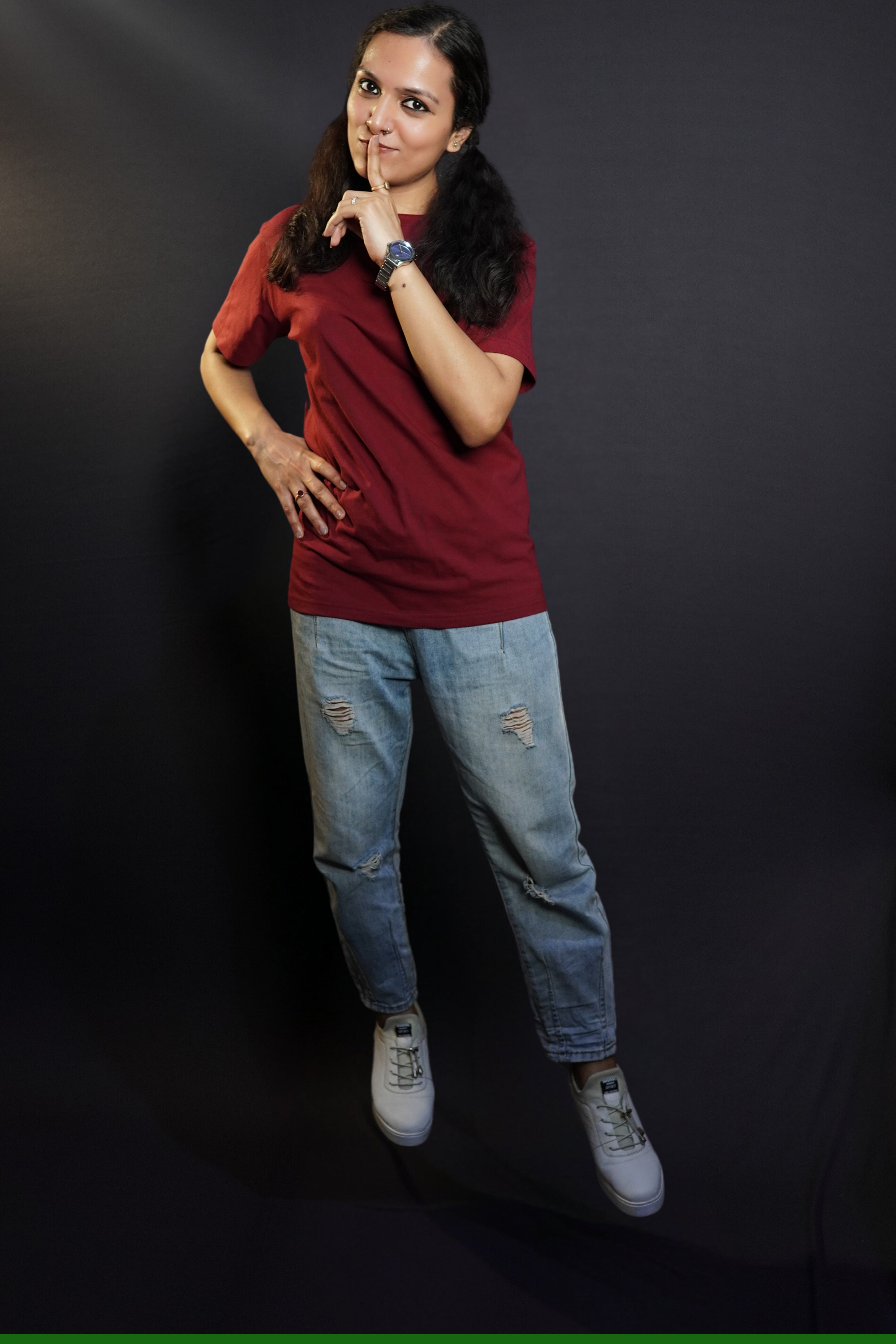A woman wearing a round neck plain moisture wicking rich maroon t-shirt, posing with her finger on her lips and hand on her waist, highlighting a swank up to the minute look-Muselot