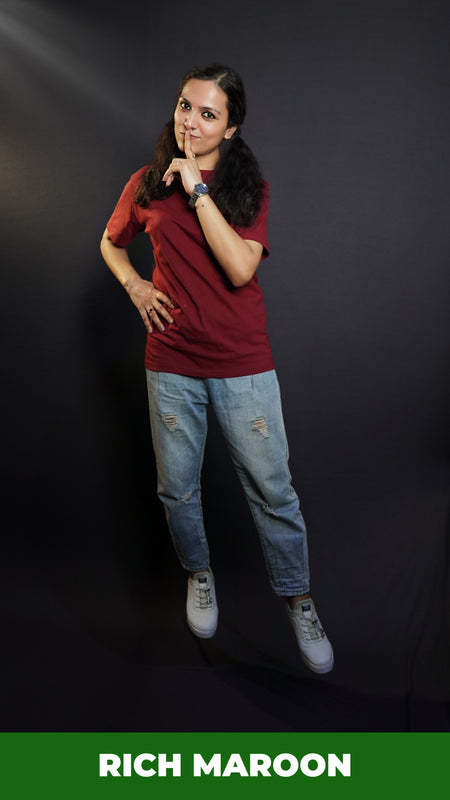 A woman wearing a round neck plain moisture wicking rich maroon t-shirt, posing with her finger on her lips and hand on her waist, highlighting a swank up to the minute look-Muselot