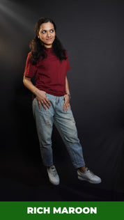 A woman wearing a short sleeved cotton stretchable rich maroon t-shirt, posing with her thumb inside the front pockets of her jeans, highlighting a stylish relaxed fit-Muselot