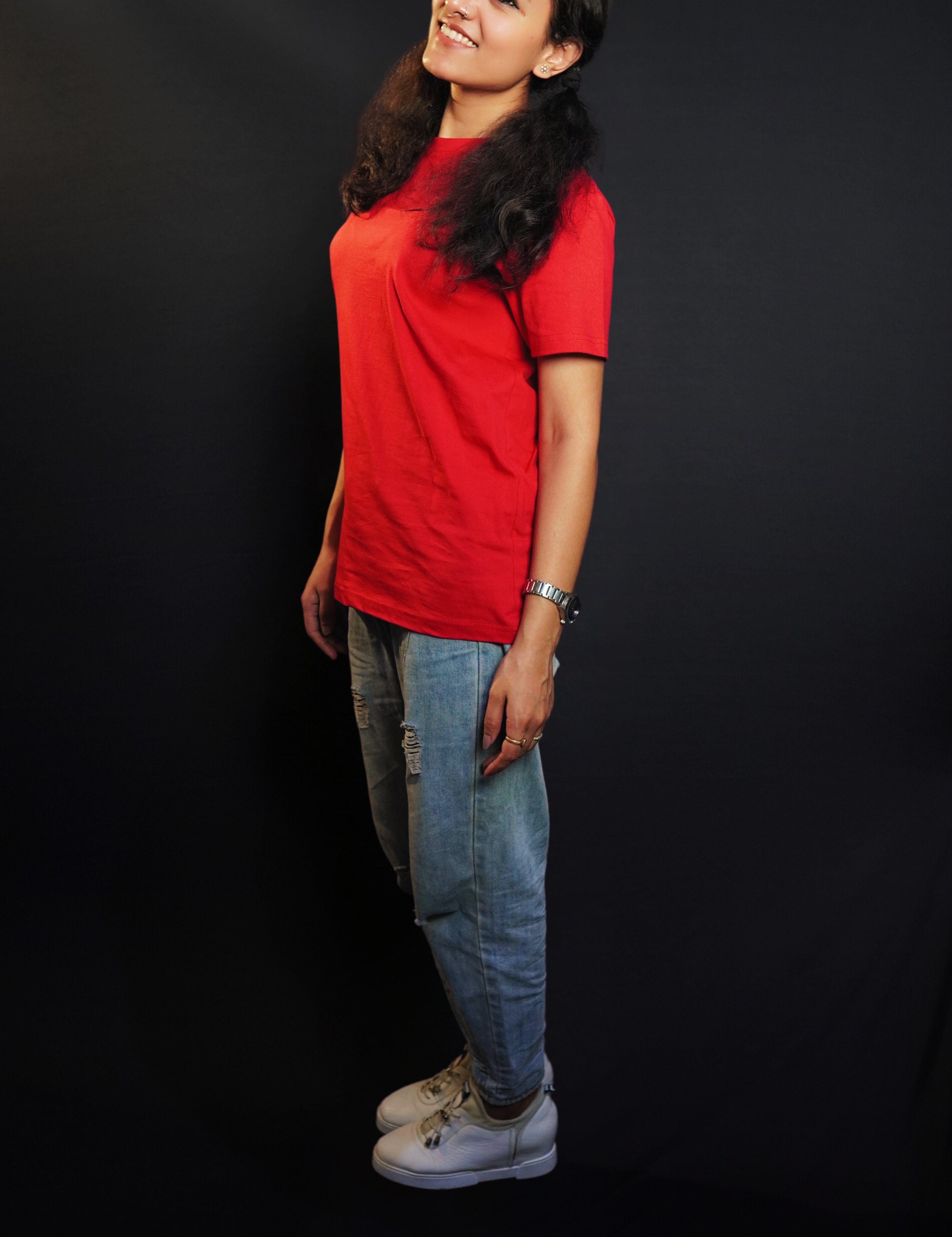 A woman standing sideways as her head bends slightly to the camera, smile on her lips, wearing a cotton round neck moisture wicking short sleeved rosy red t-shirt, highlighting a modish loose fit-Muselot