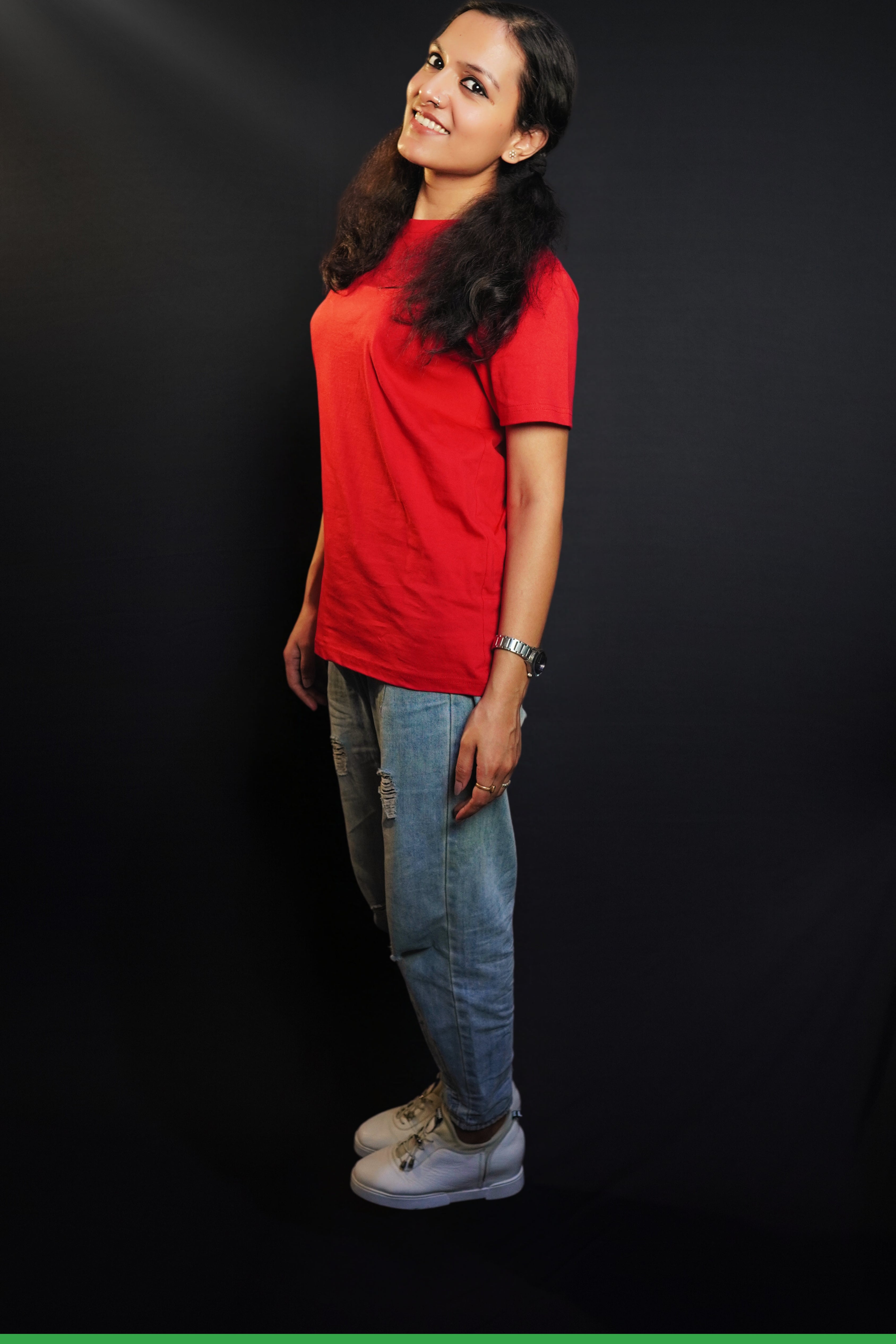 A woman standing sideways as her head bends slightly to the camera, smile on her lips, wearing a cotton round neck moisture wicking short sleeved rosy red t-shirt, highlighting a modish loose fit-Muselot