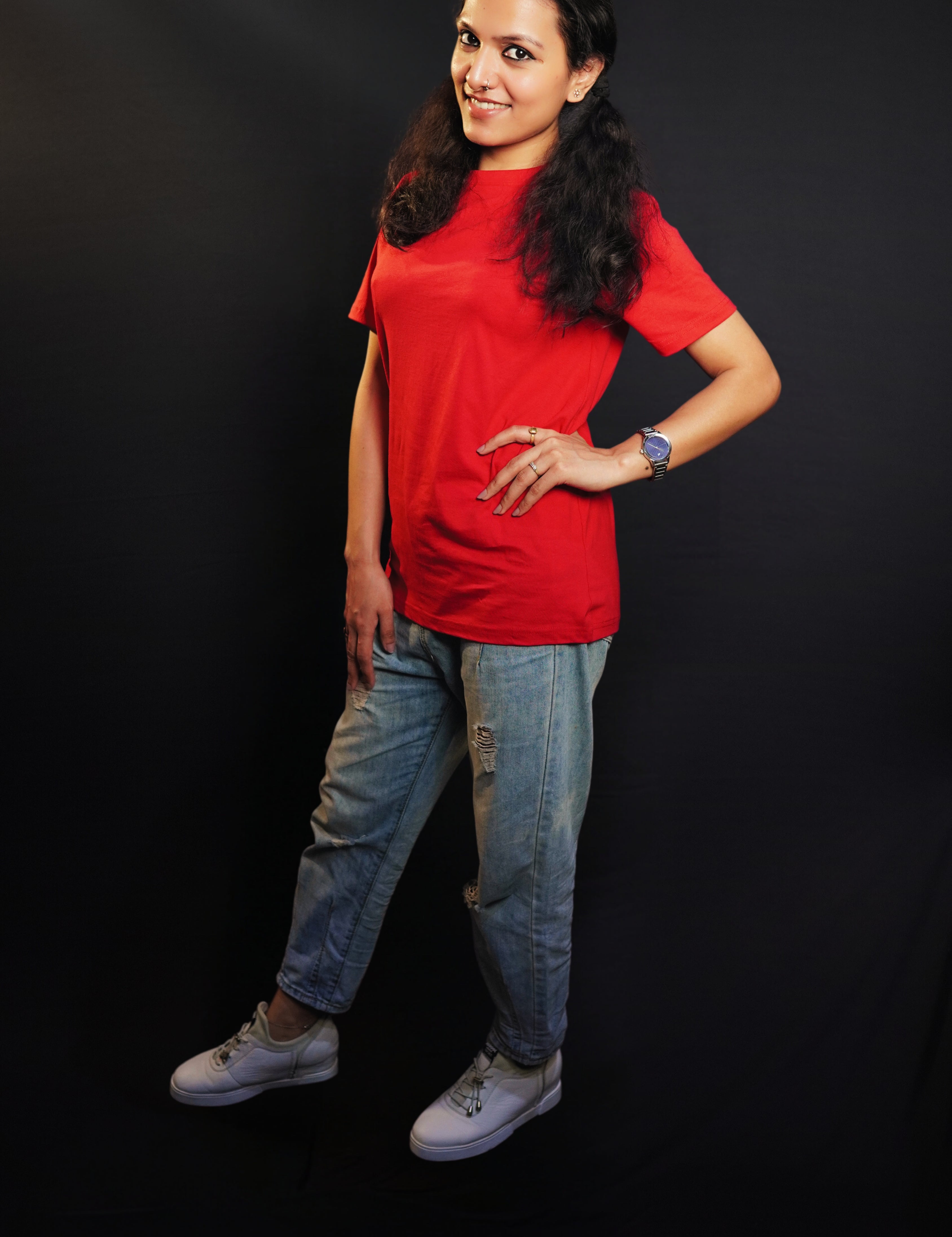 A woman wearing a long length short sleeved moisture wicking rosy red t-shirt, posing with her hands on her waist and other hanging on her side as she stand sideways against a dark background, highlighting a trendy in vogue look-Muselot