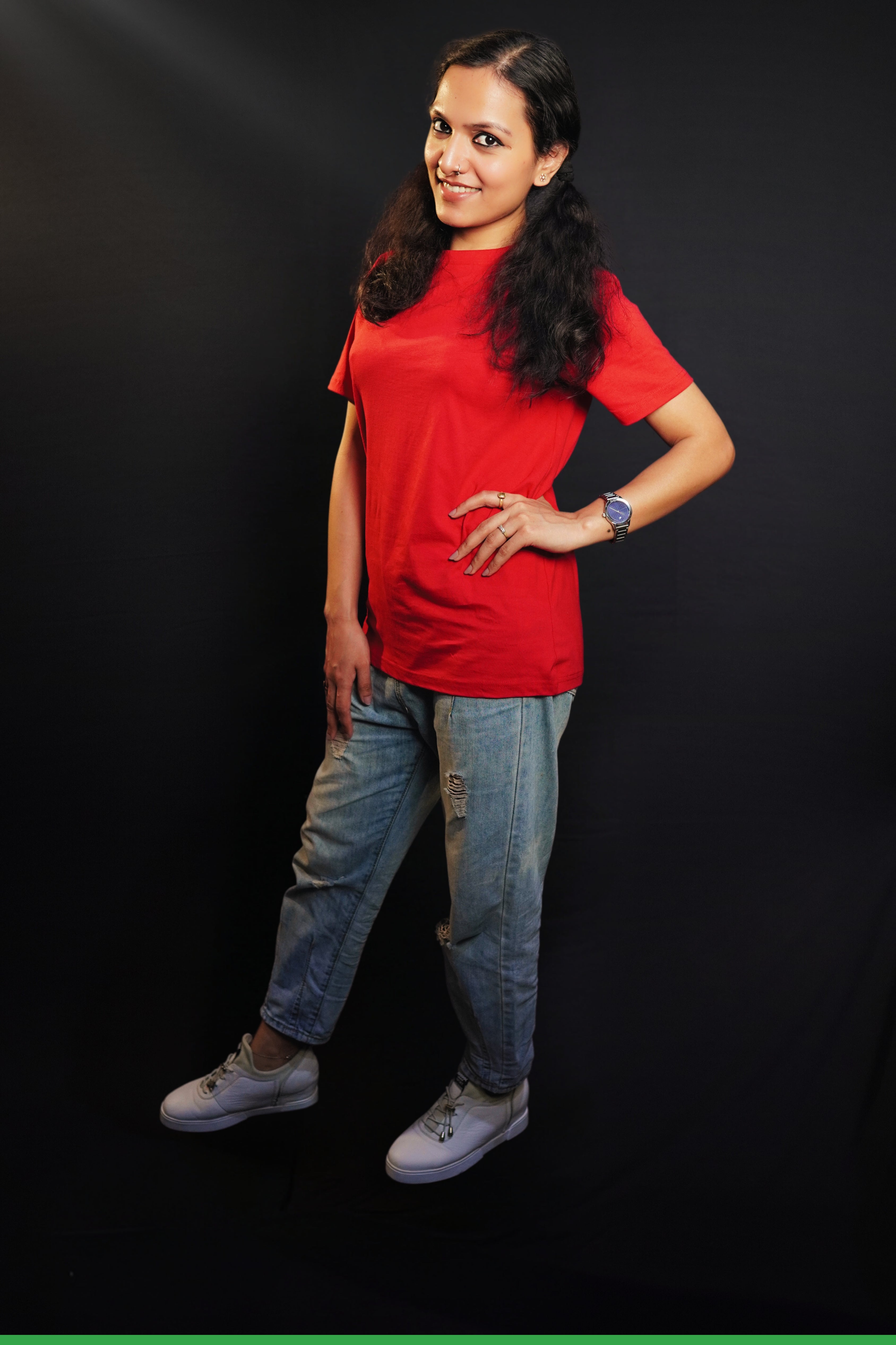 A woman wearing a long length short sleeved moisture wicking rosy red t-shirt, posing with her hands on her waist and other hanging on her side as she stand sideways against a dark background, highlighting a trendy in vogue look-Muselot