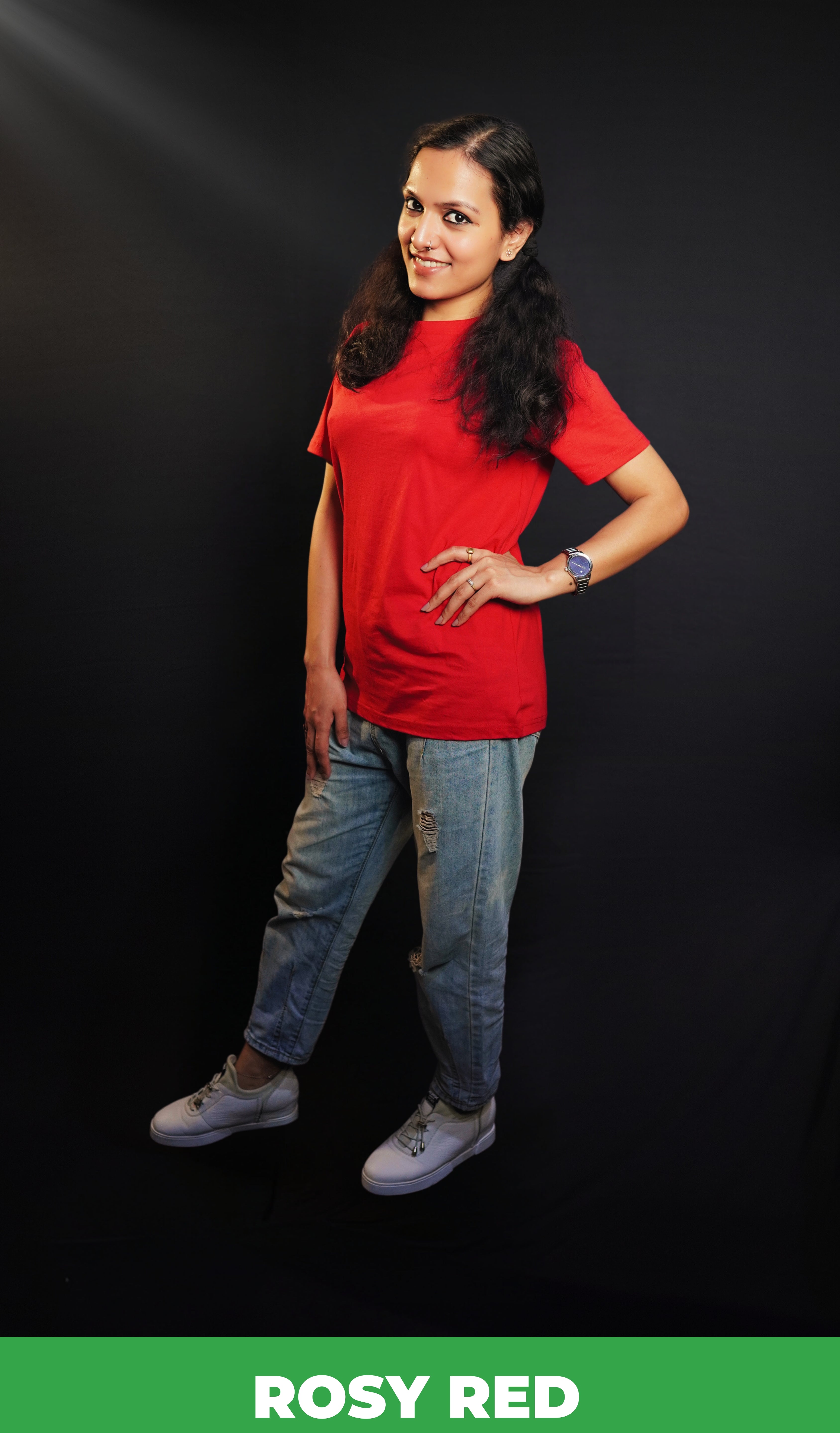 A woman wearing a long length short sleeved moisture wicking rosy red t-shirt, posing with her hands on her waist and other hanging on her side as she stand sideways against a dark background, highlighting a trendy in vogue look-Muselot