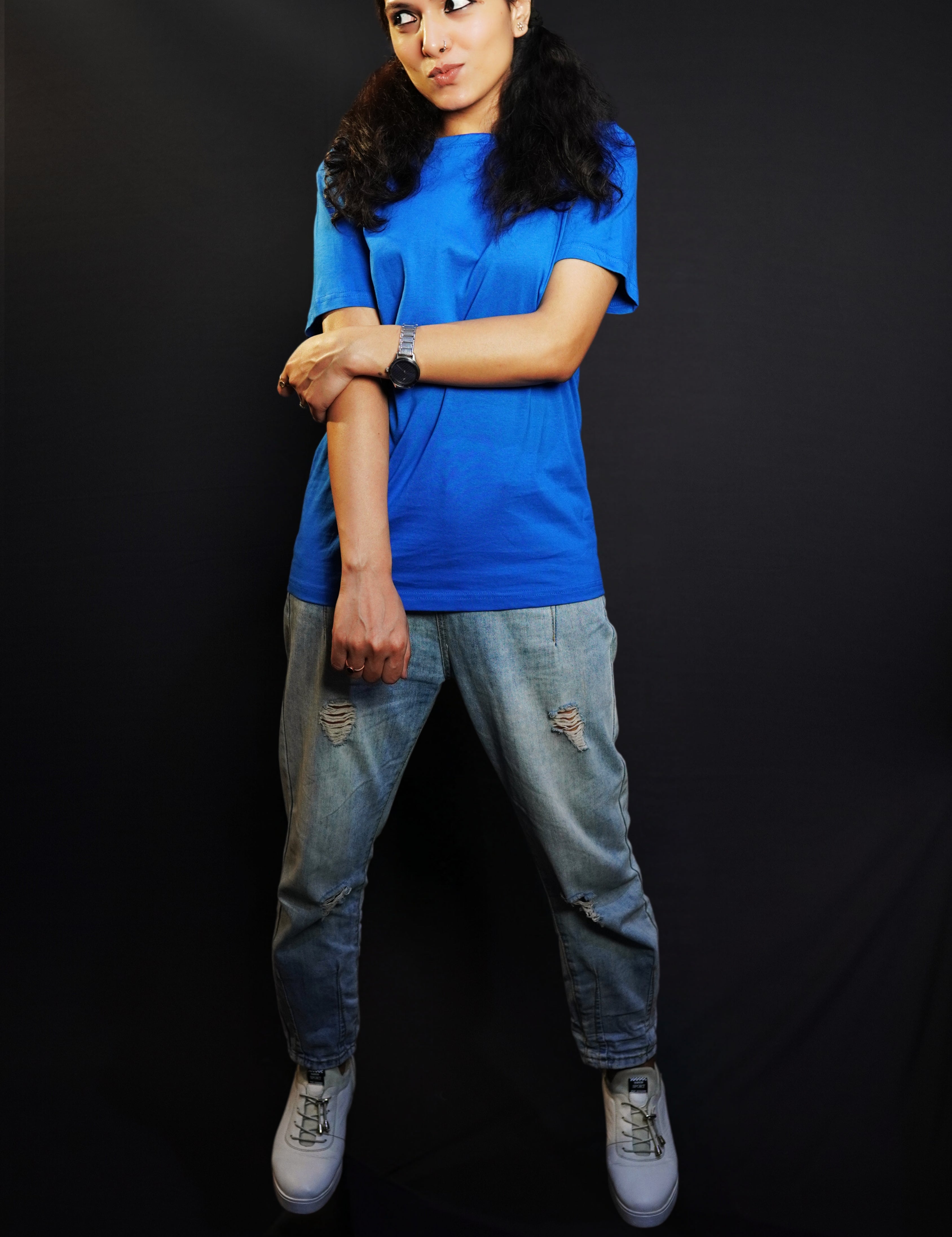 A woman wearing a stretchable round neck long length plain royal blue t-shirt, posing with her hand grabbing another that is hanging in front of her, pouting a little, highlighting a swank flowing fit-Muselot