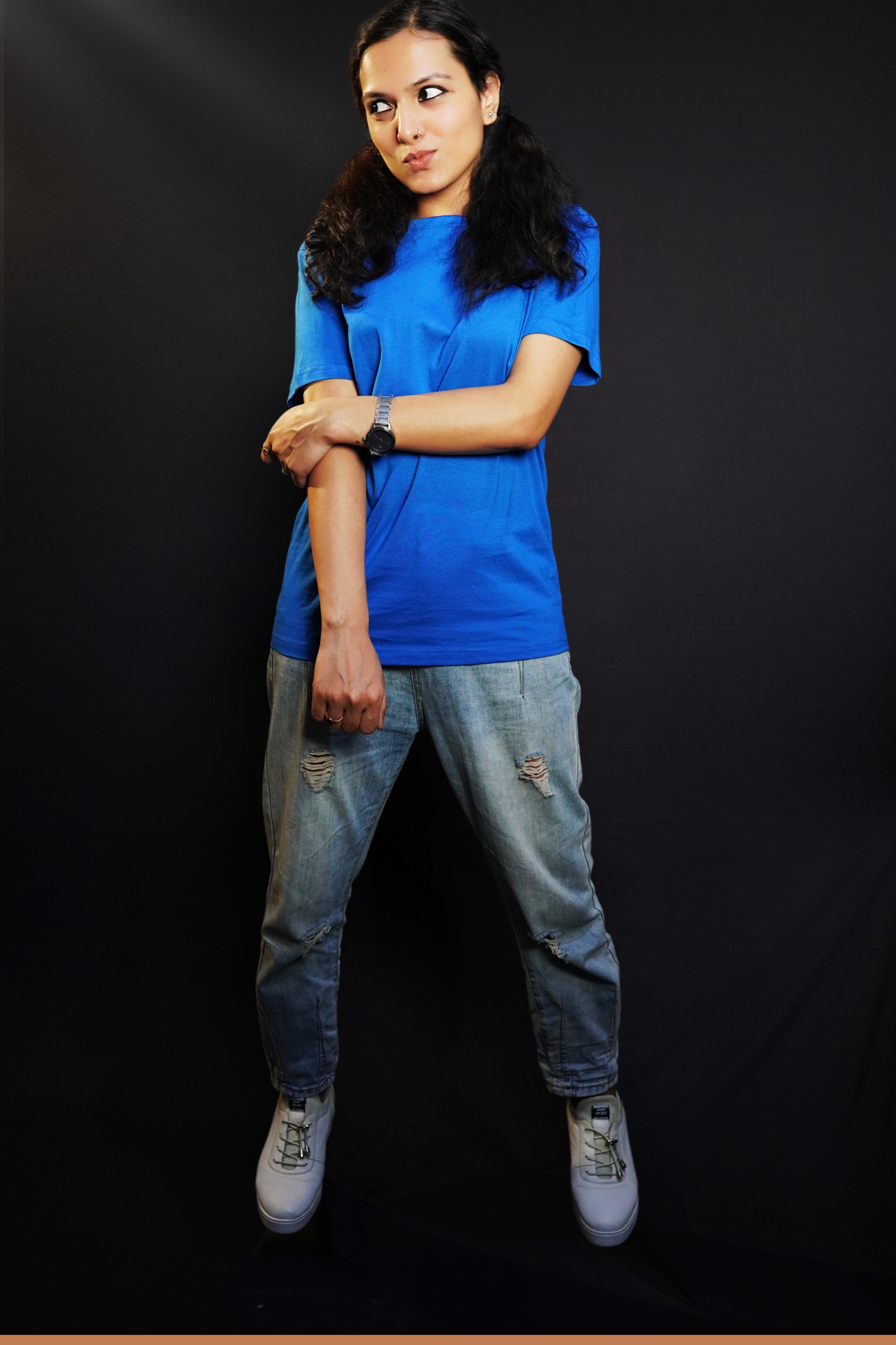 A woman wearing a stretchable round neck long length plain royal blue t-shirt, posing with her hand grabbing another that is hanging in front of her, pouting a little, highlighting a swank flowing fit-Muselot