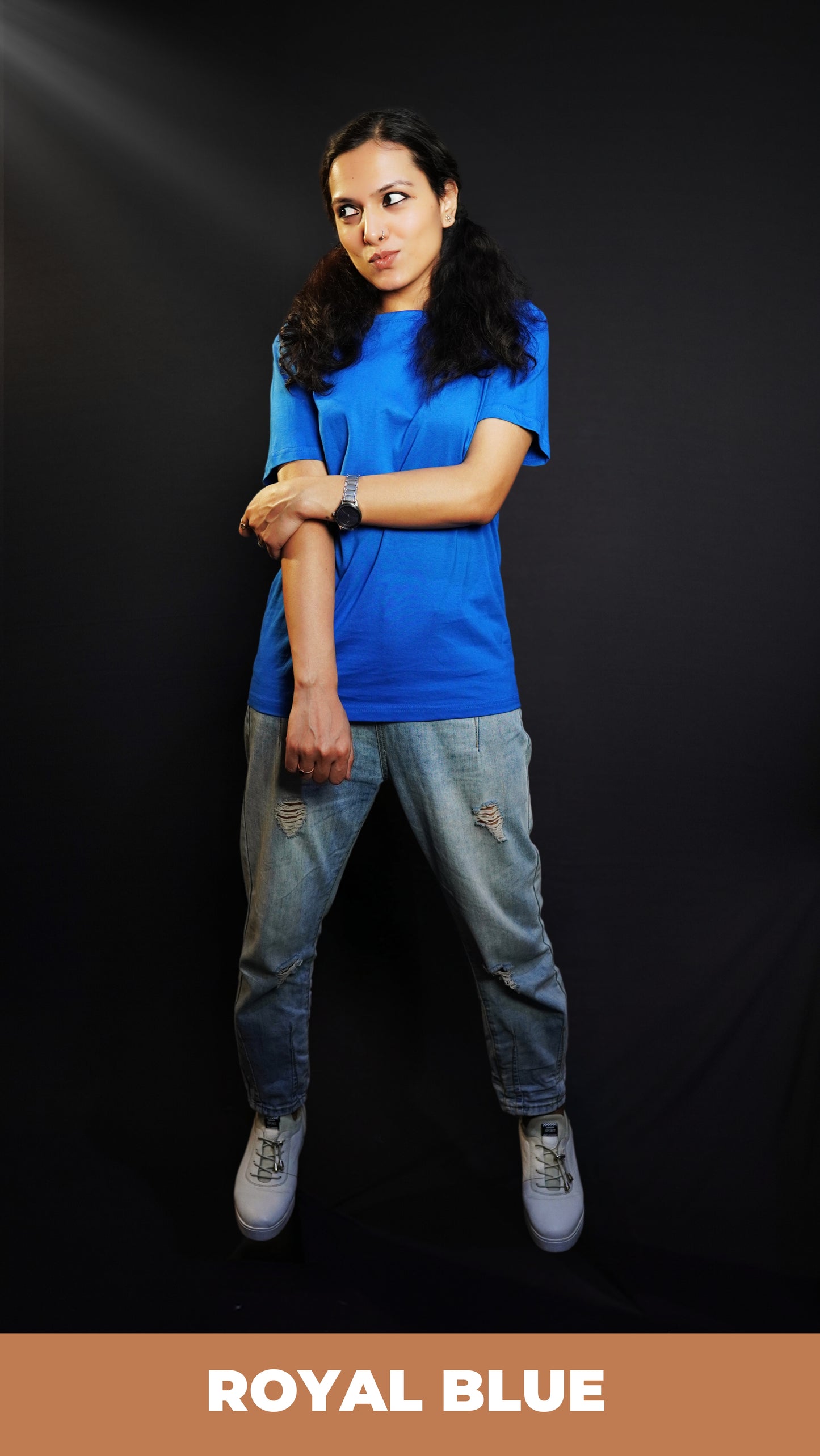 A woman wearing a stretchable round neck long length plain royal blue t-shirt, posing with her hand grabbing another that is hanging in front of her, pouting a little, highlighting a swank flowing fit-Muselot