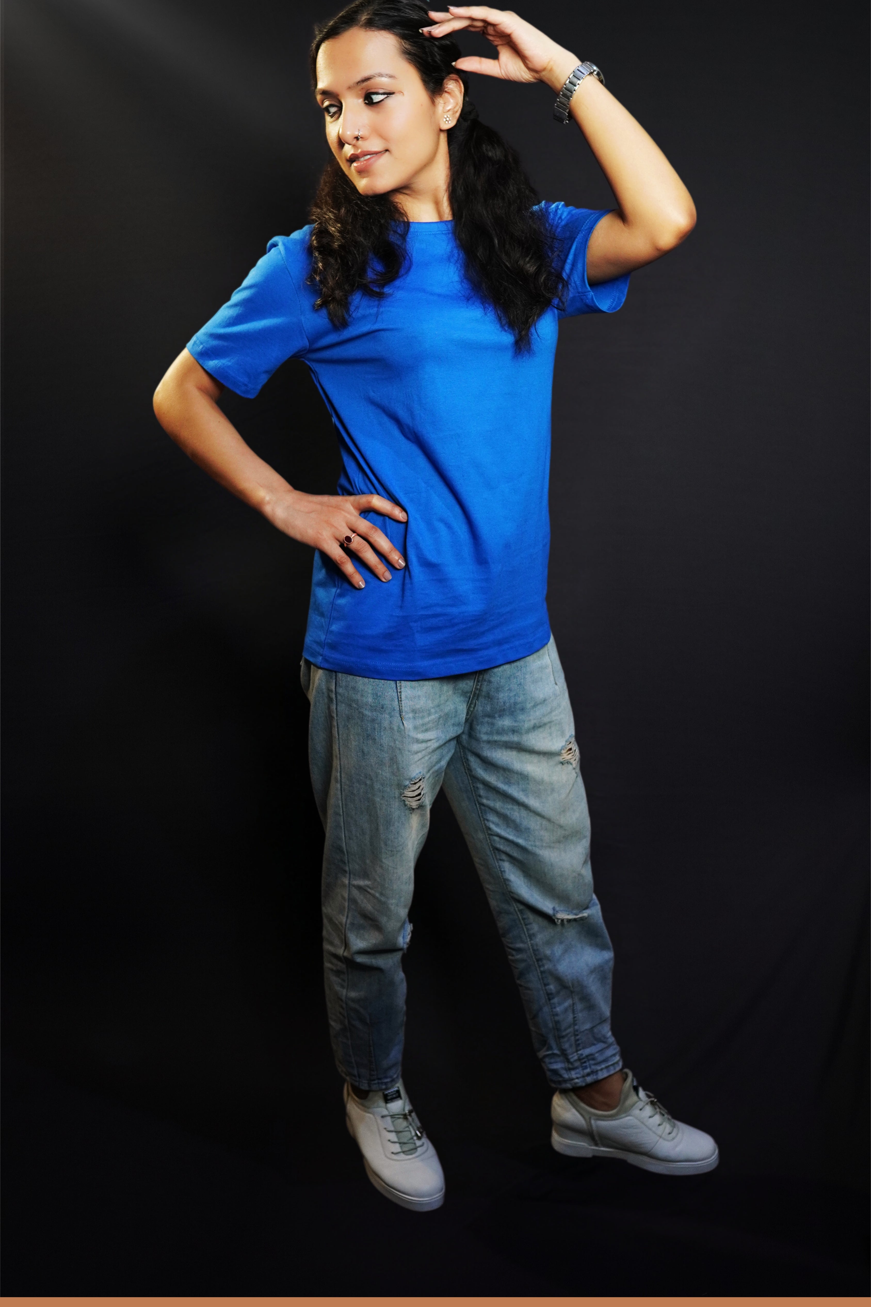 A woman wearing a unisex plain cotton round neck royal blue t-shirt, posing with her hand on her head and another on her waist as she looks sideways, highlighting a summer casual fit-Muselot