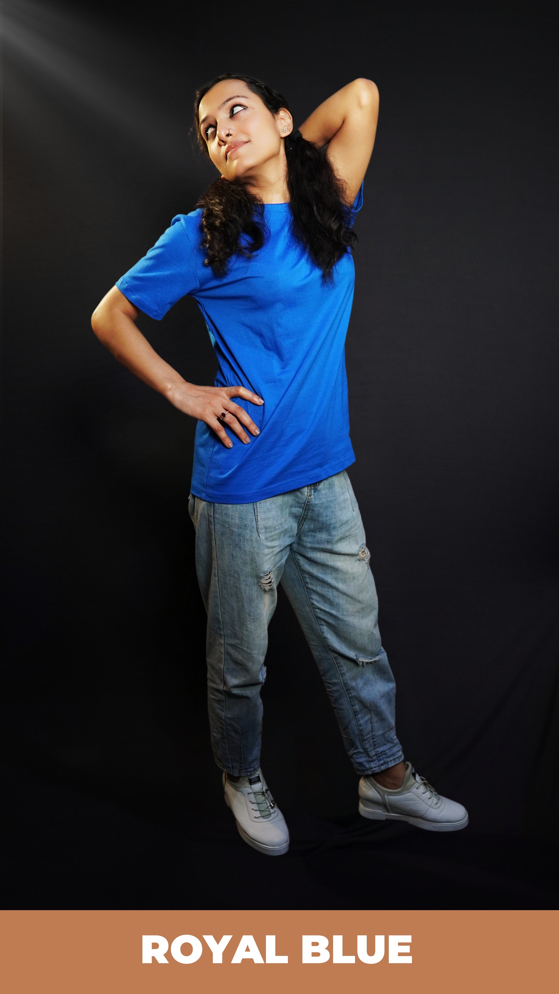 A stylish model wearing a long length adult's plain round neck royal blue t-shirt, posing with her hand up touching her back and another on her waist, showcasing an aesthetic cozy look-Muselot