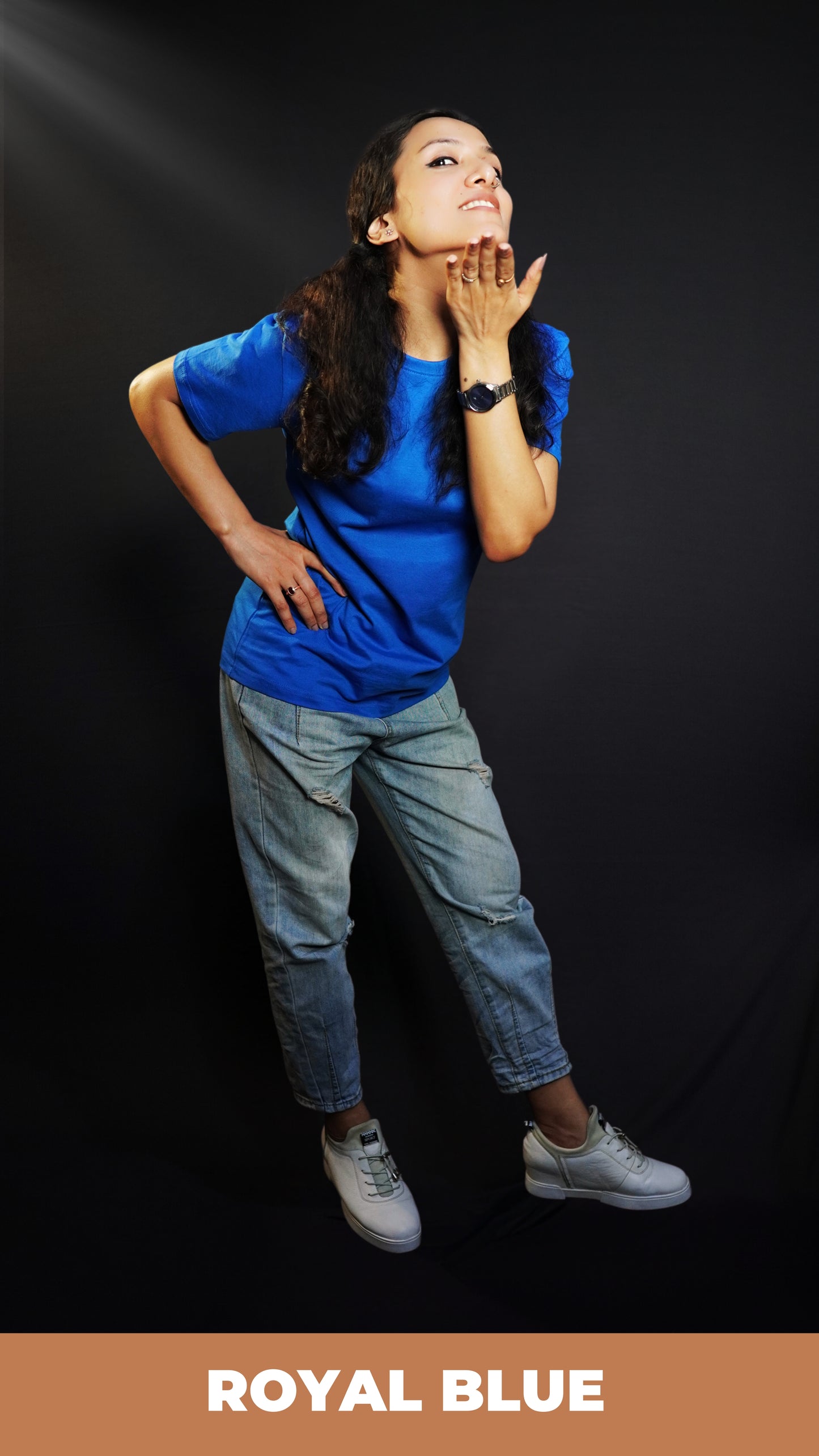 A pretty woman posing with her hand under her chin and other on her waist bending slightly forward, wearing a long length girl's moisture wicking royal blue t-shirt, highlighting a relaxed casual fit-Muselot