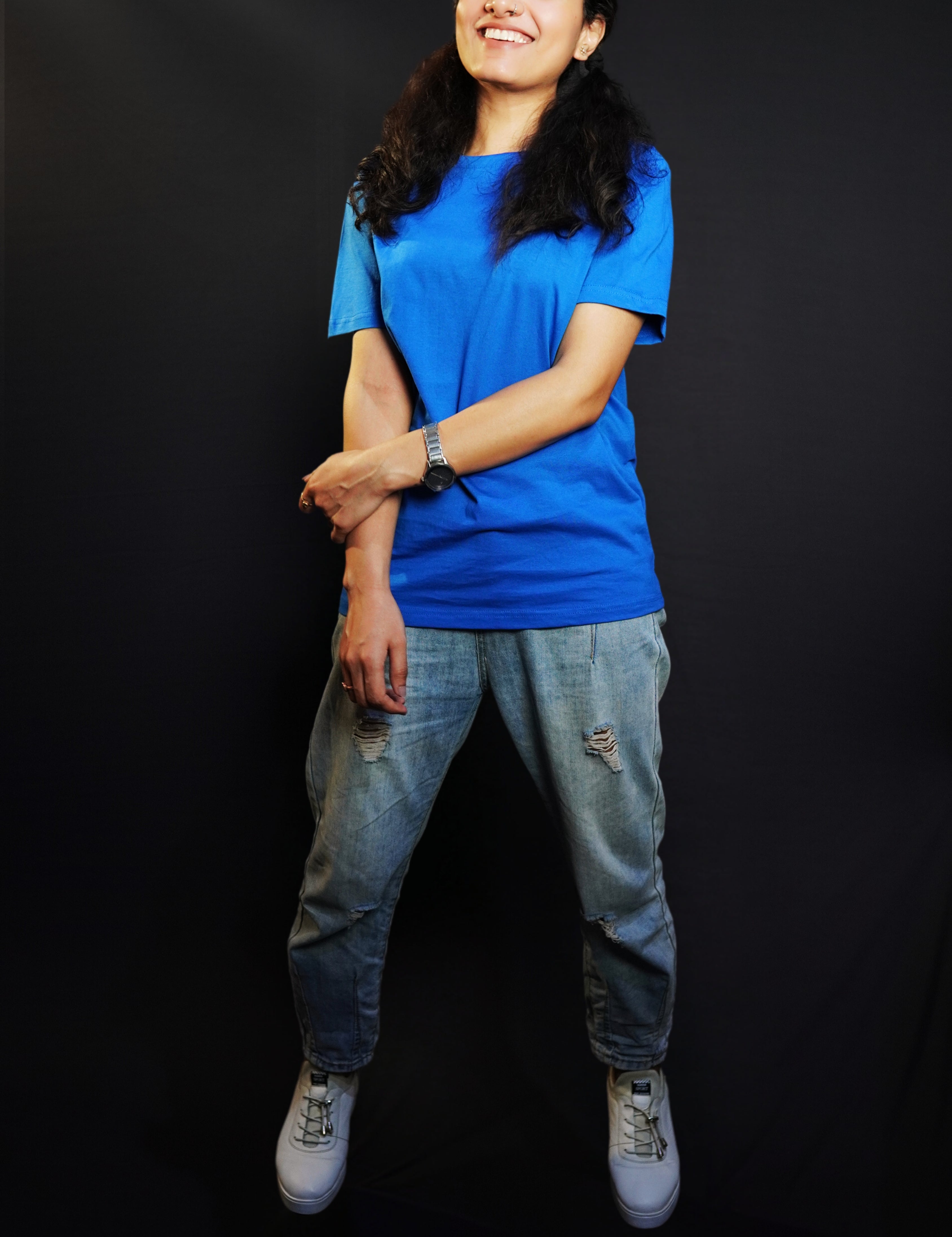 A woman smiling happily posing with her hand grabbing her forearm, wearing a long length royal blue plain round neck t-shirt, showcasing a popular easygoing fit-Muselot