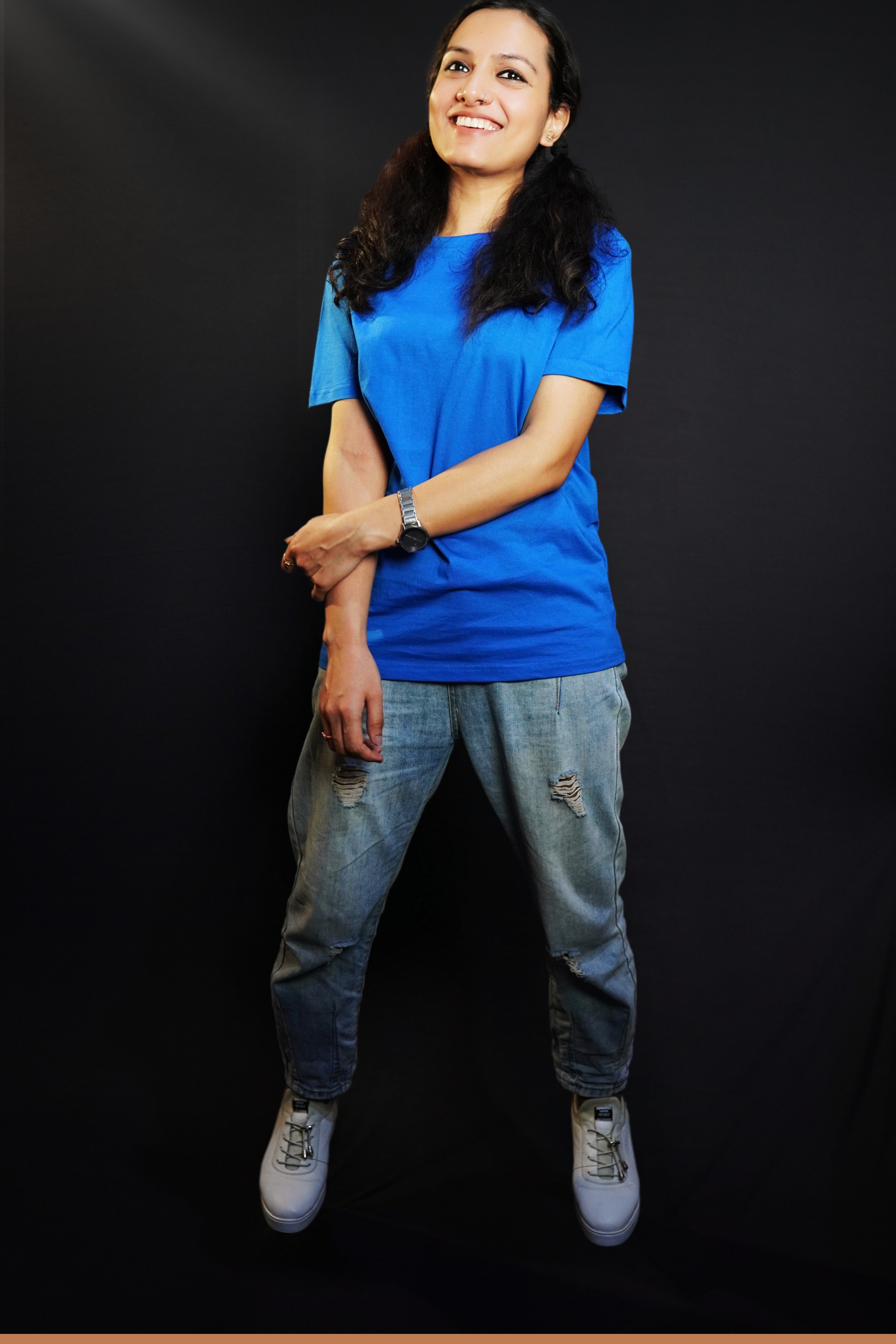 A woman smiling happily posing with her hand grabbing her forearm, wearing a long length royal blue plain round neck t-shirt, showcasing a popular easygoing fit-Muselot