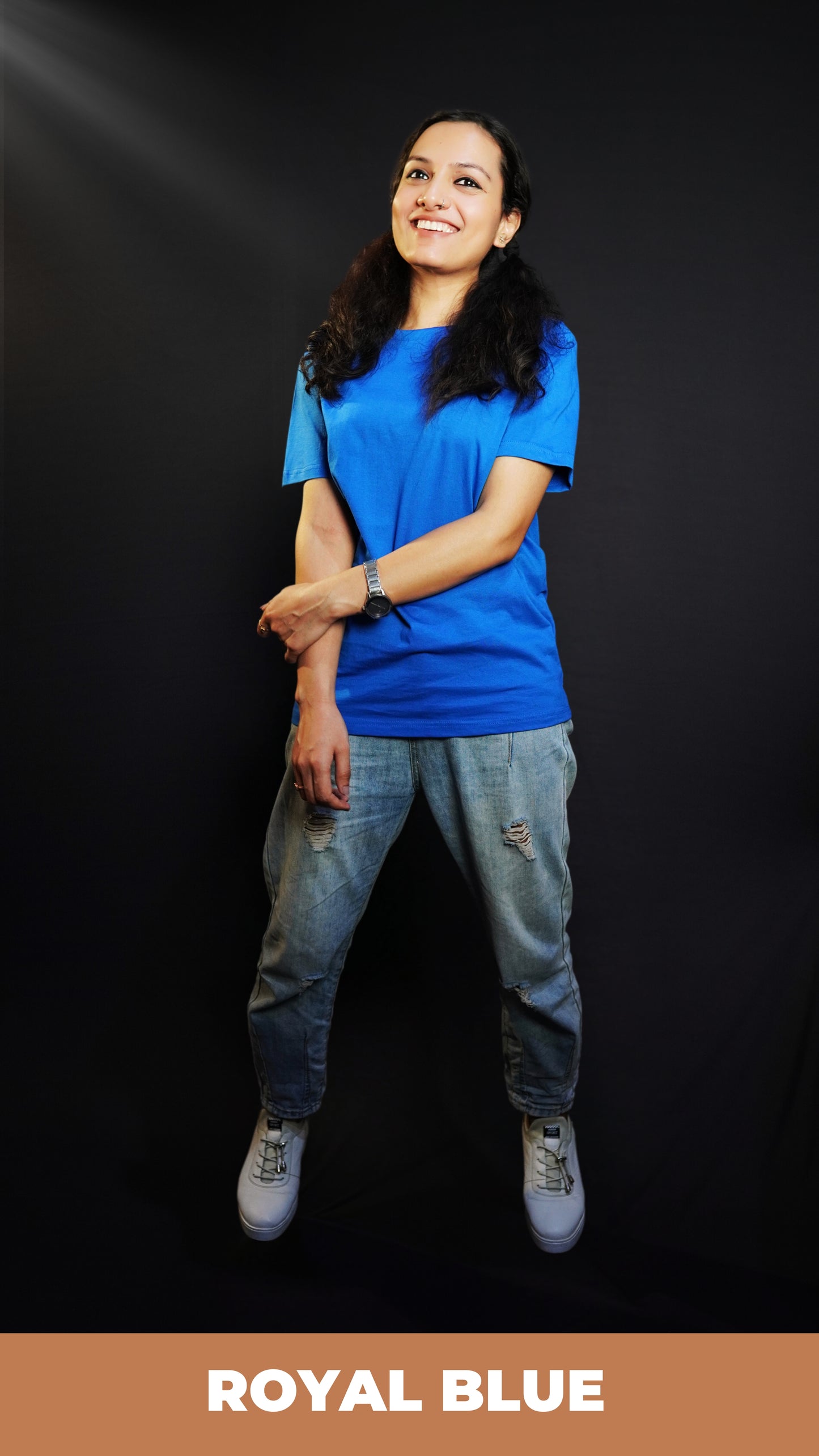 A woman smiling happily posing with her hand grabbing her forearm, wearing a long length royal blue plain round neck t-shirt, showcasing a popular easygoing fit-Muselot