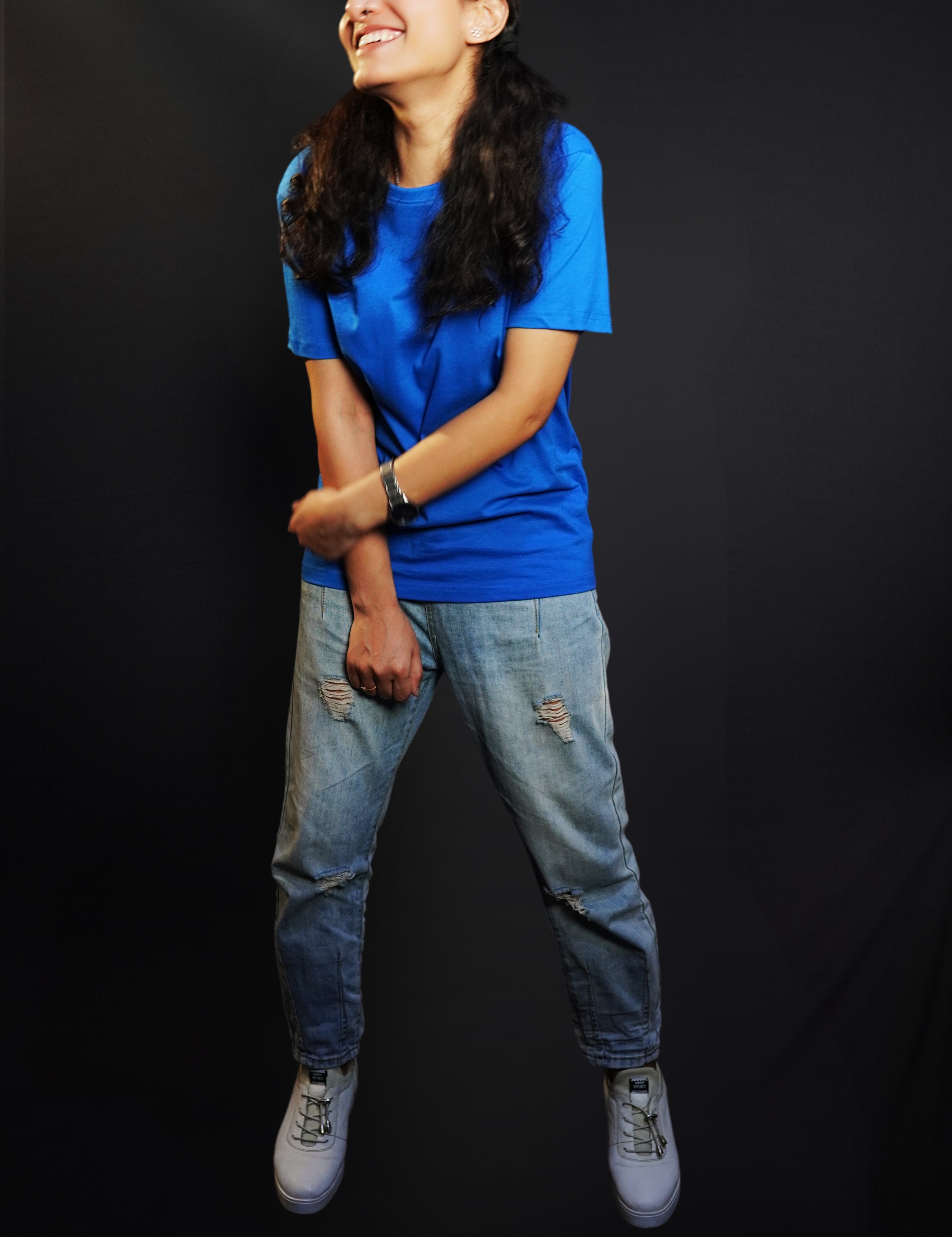A woman laughing out loud with her hand grabbing her forearm standing against a dark background, wearing a long length cotton quick drying royal blue t-shirt, highlighting an in demand relaxed look-Muselot