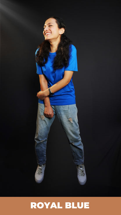 A woman laughing out loud with her hand grabbing her forearm standing against a dark background, wearing a long length cotton quick drying royal blue t-shirt, highlighting an in demand relaxed look-Muselot